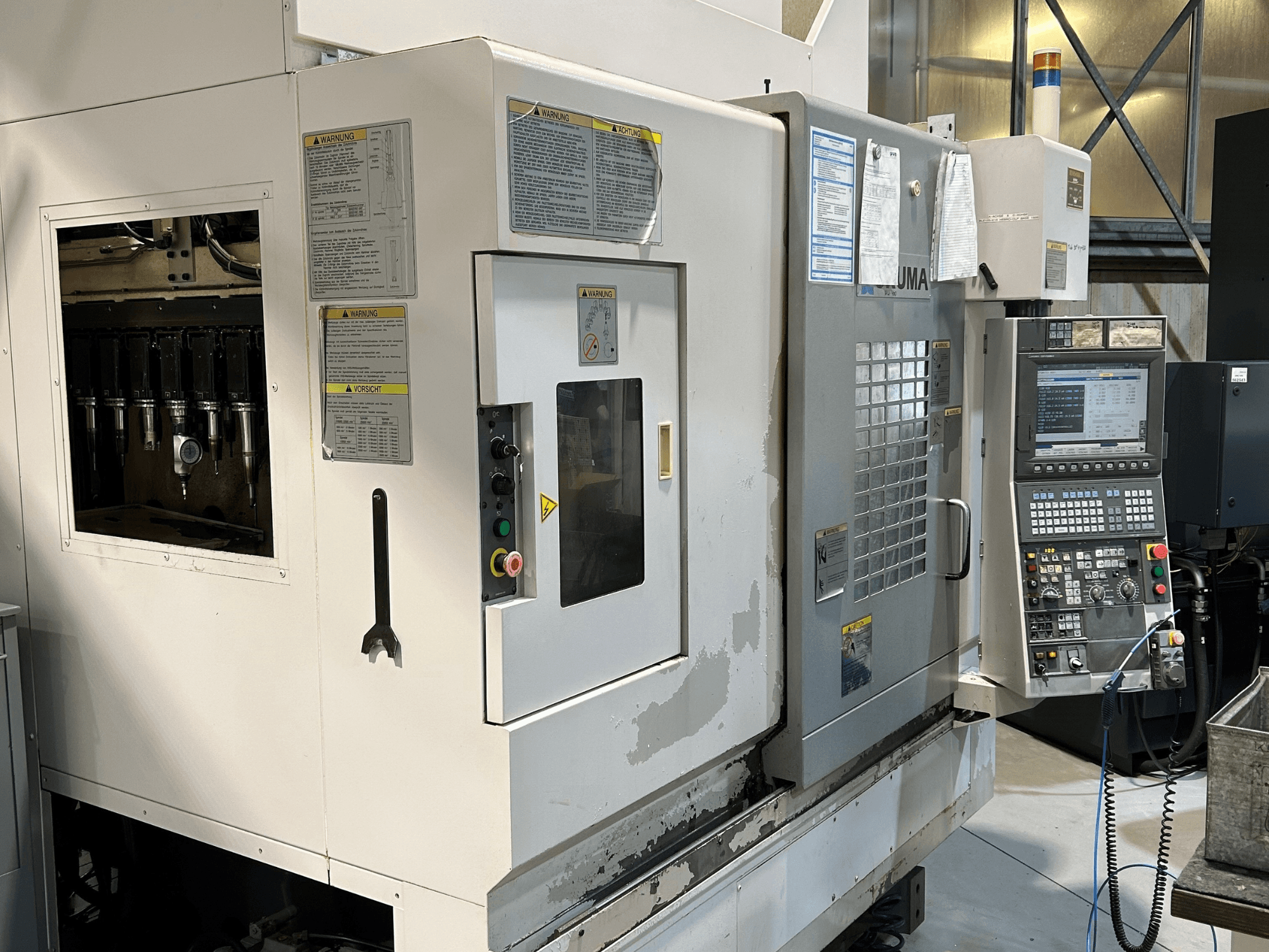 Front view of a UMA CNC machine with visible tool holders, control panel, warning labels, and operational buttons.