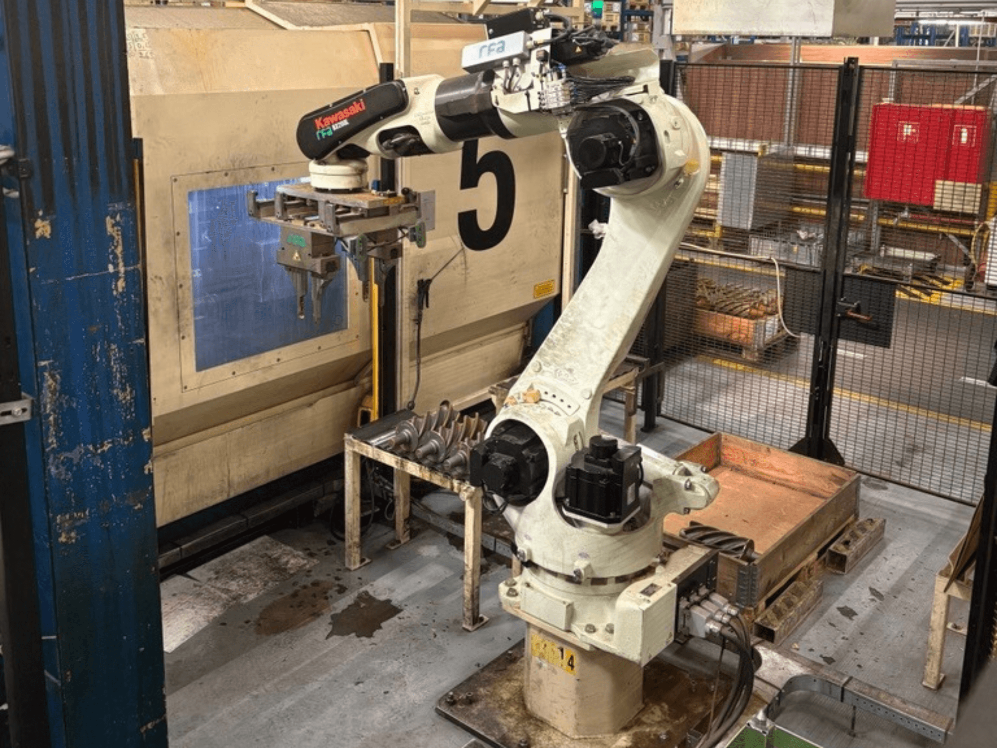 Front view of a Kawasaki E42F-A001 robot arm in an industrial setting, equipped with a gripper and situated near a worktable.