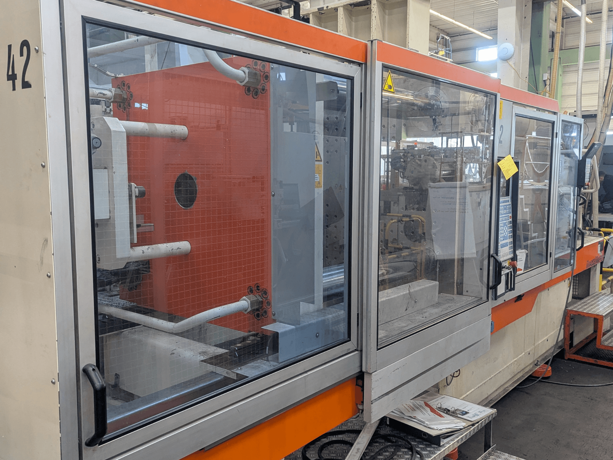 Krauss Maffei KM 350-3000 hydraulic injection moulding machine, side view showing controls and internal components behind glass panel.