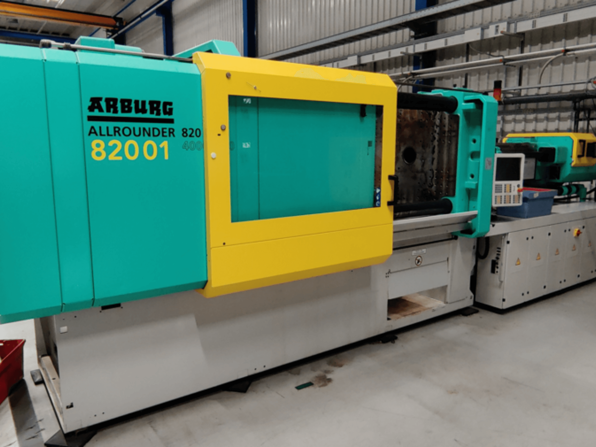 Arburg ALLROUNDER 82001 injection molding machine in teal and yellow, side view showcasing control panel and operational features.