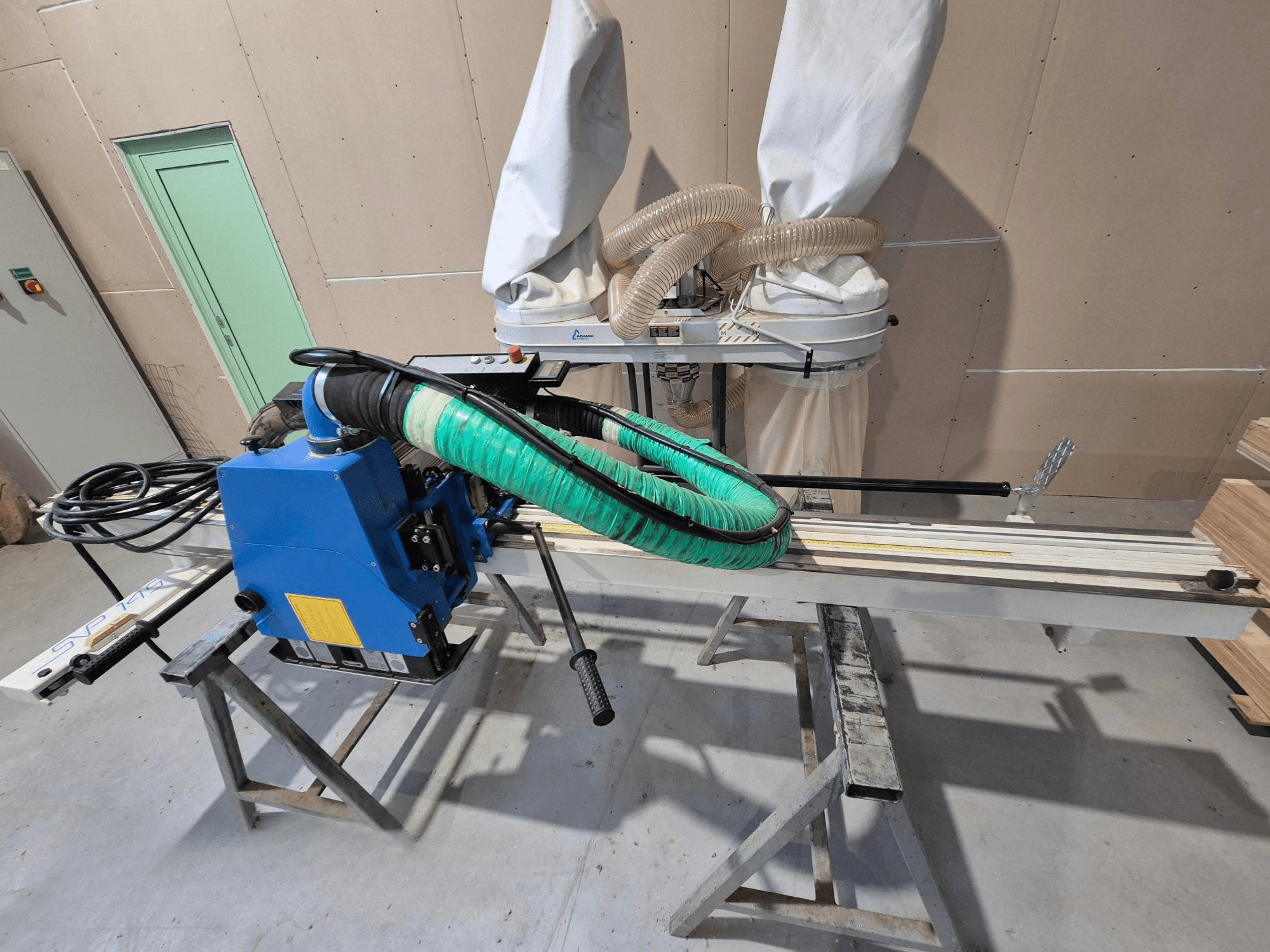 Blue SVP-175 horizontal panel saw with green dust hose and support, viewed from the side in a workshop setting.