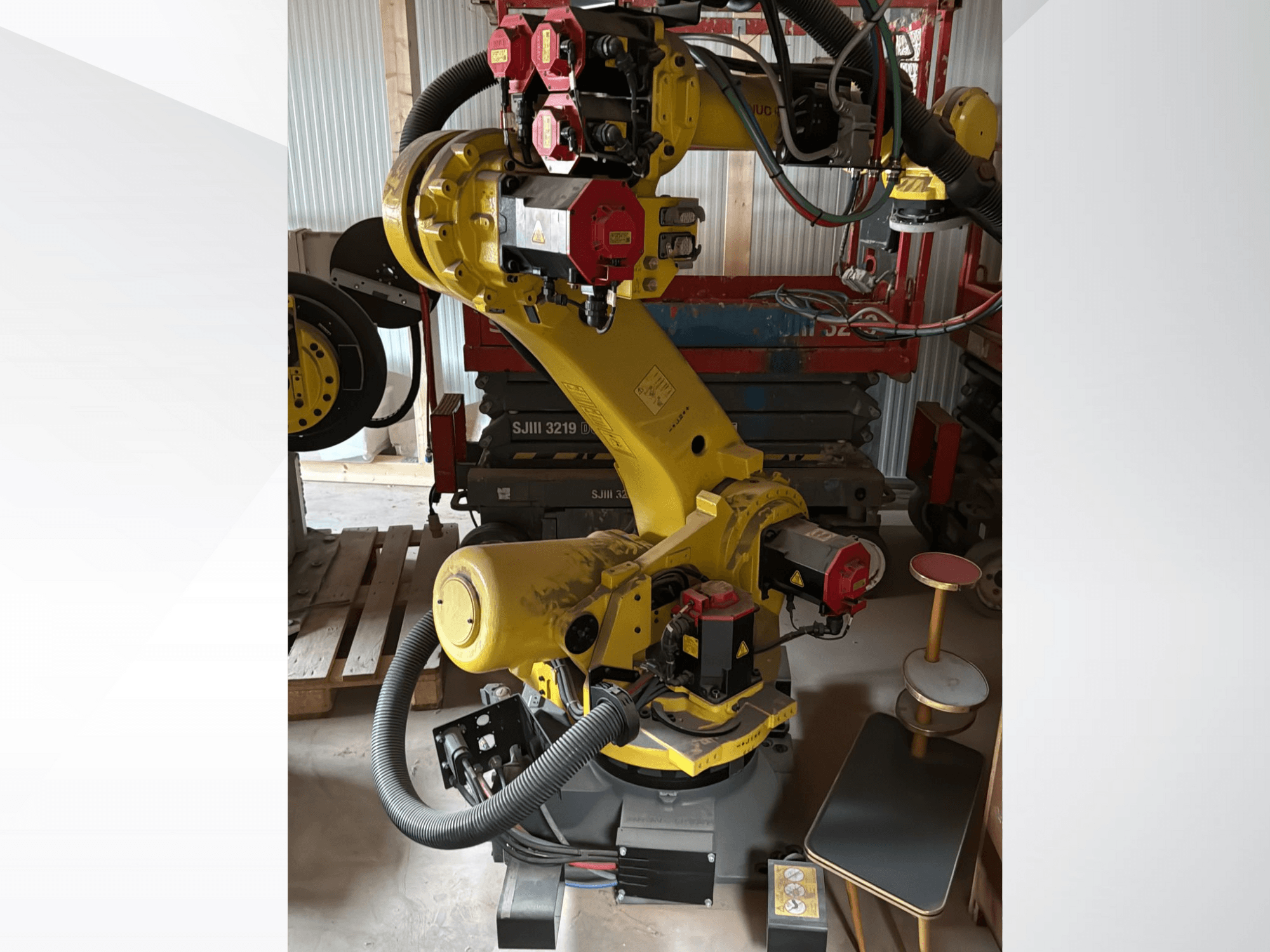 Yellow industrial robotic arm with red controllers, front view; features multiple joints and hoses, set on a worksite.