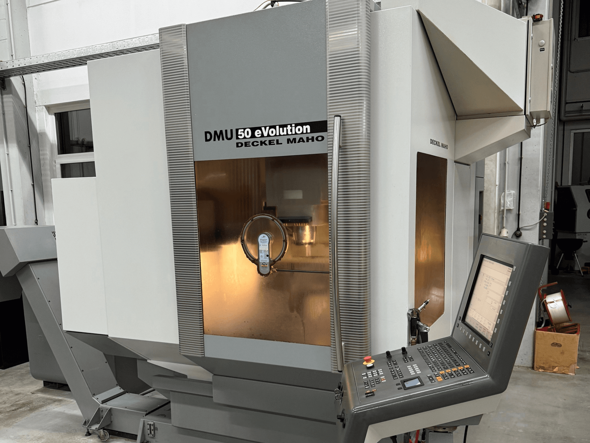 DMU 50 eVOLUTION by Deckel Maho, front view of CNC milling machine with control panel, shiny surface, and tool holder visible.