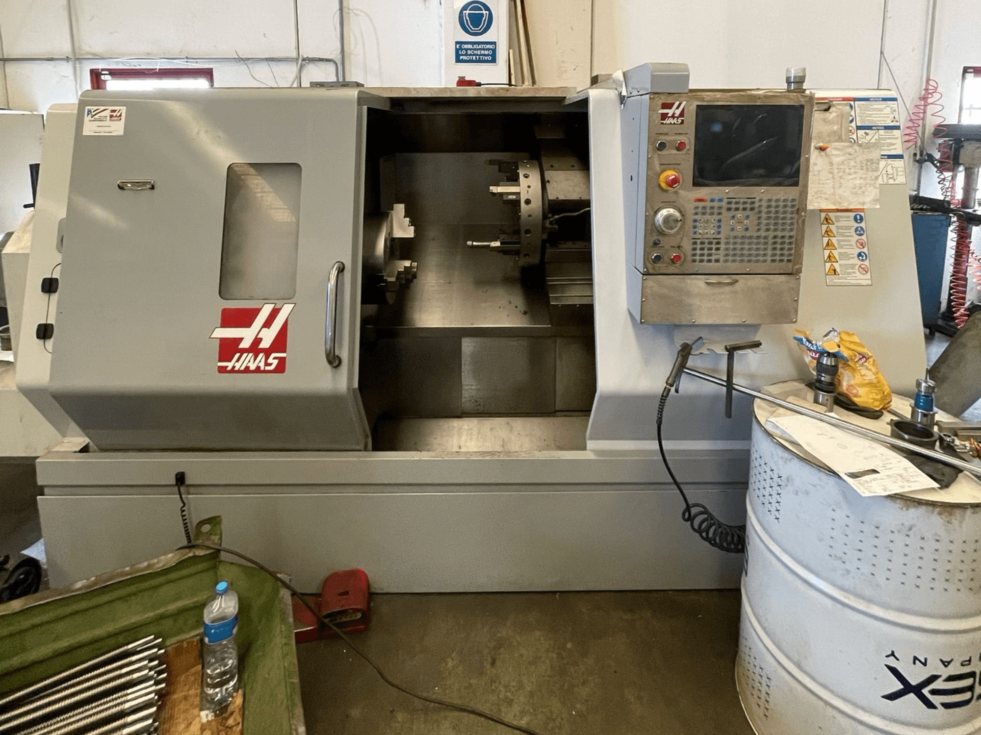 HAAS SL-30TBHE horizontal turning machine in front view, with control panel, large loading door, and various tools nearby.