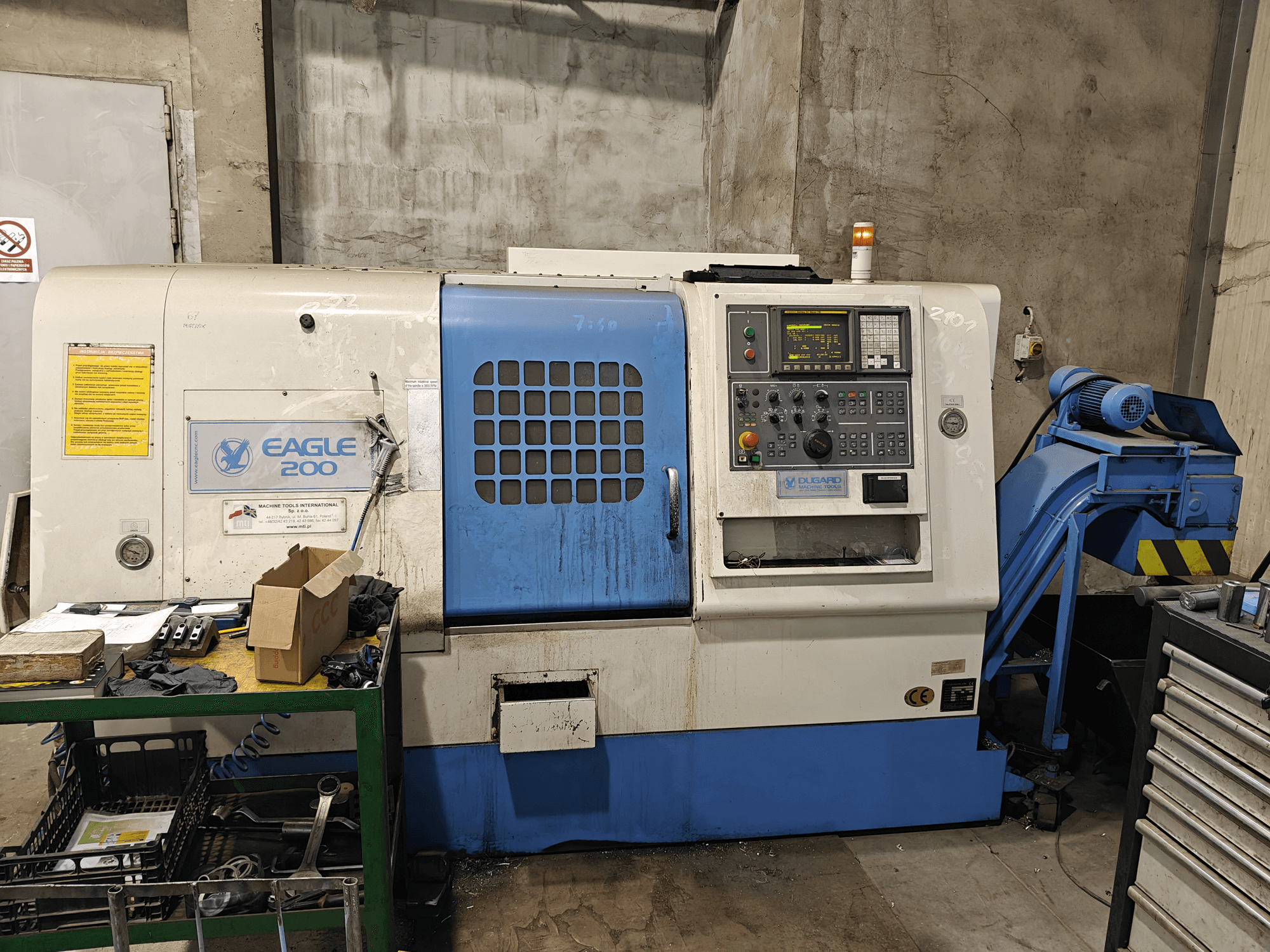 Eagle 200 CNC machine, front view with control panel, various tools on a green cart. Visible wear and operational lights.