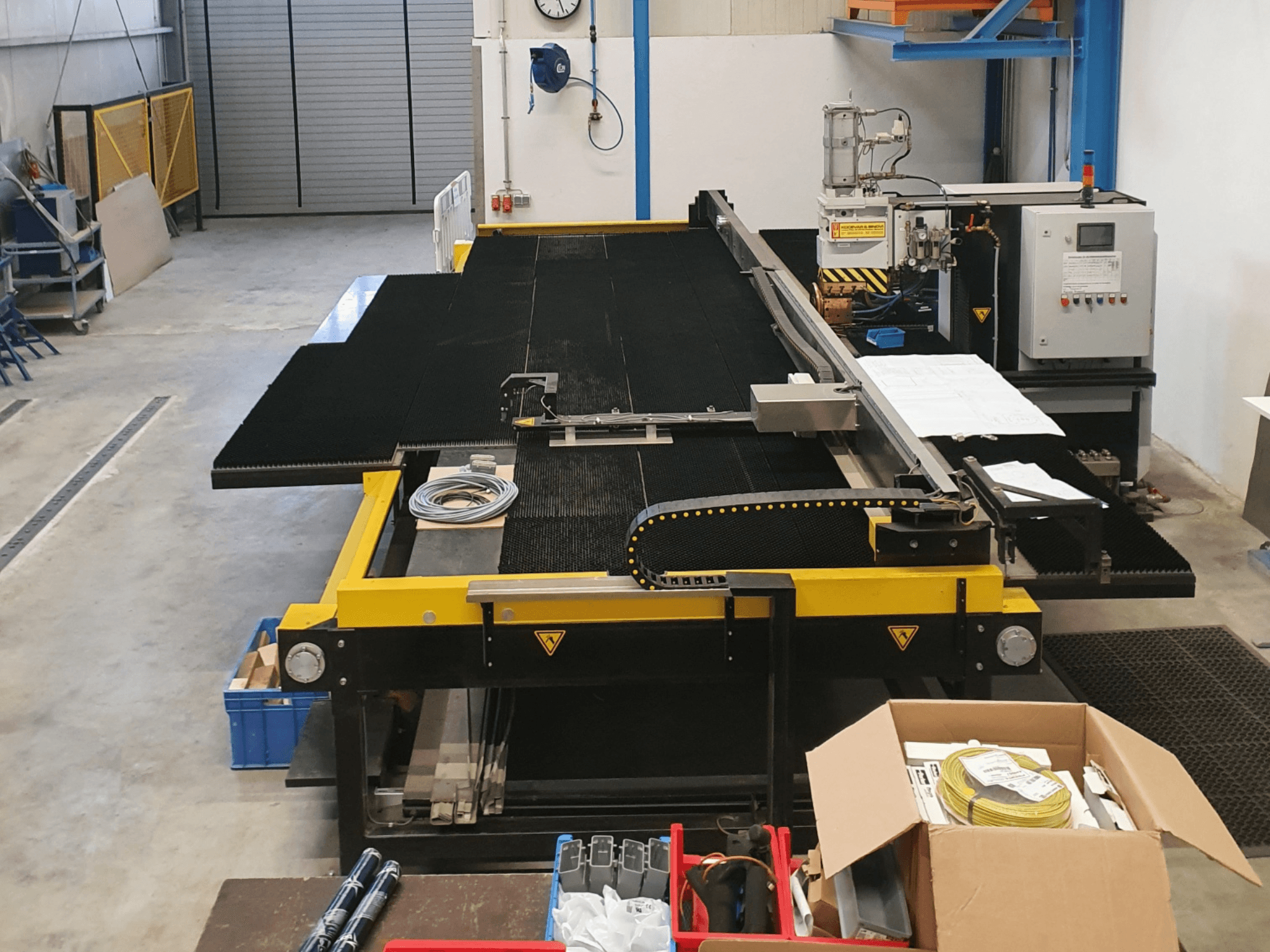 Industrial cutting machine with yellow and black features, front view, showing controls and accessories in a factory setting.