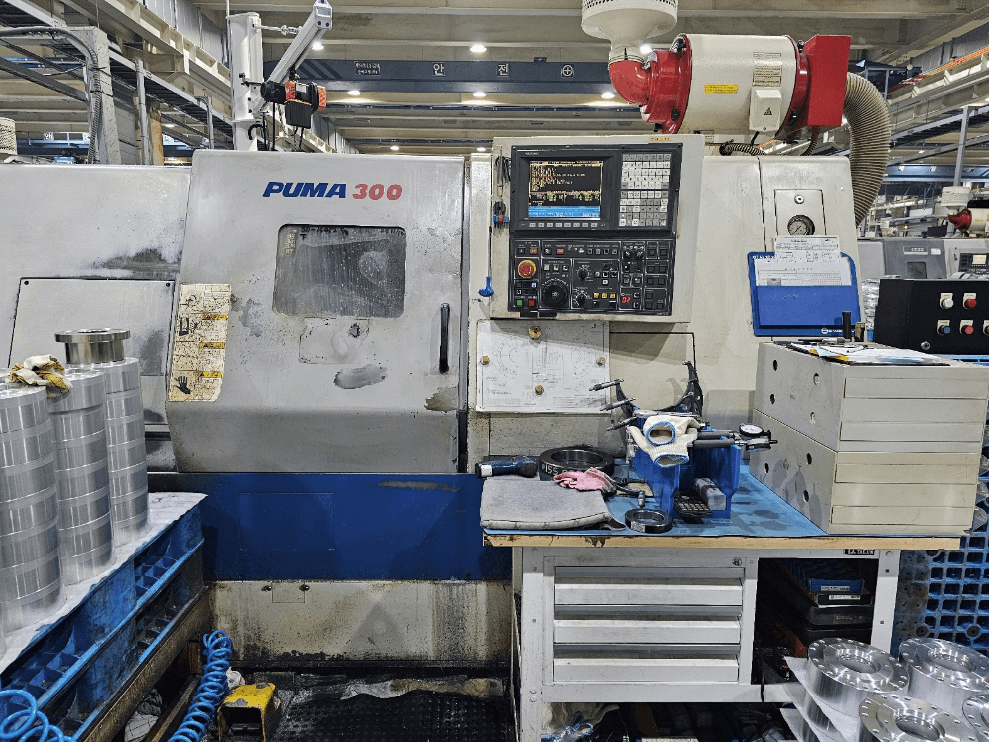 PUMA 300 CNC machine in a workshop; front view showing control panel, tools, and metal parts on a workbench.