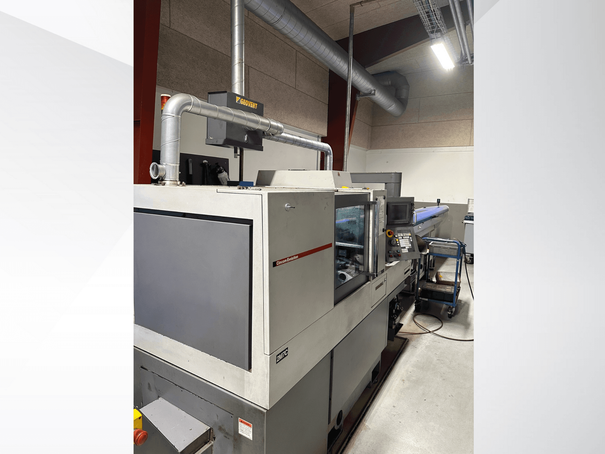 Industrial machinery from the brand MVC, side view with control panel and ductwork visible, set in a factory environment.