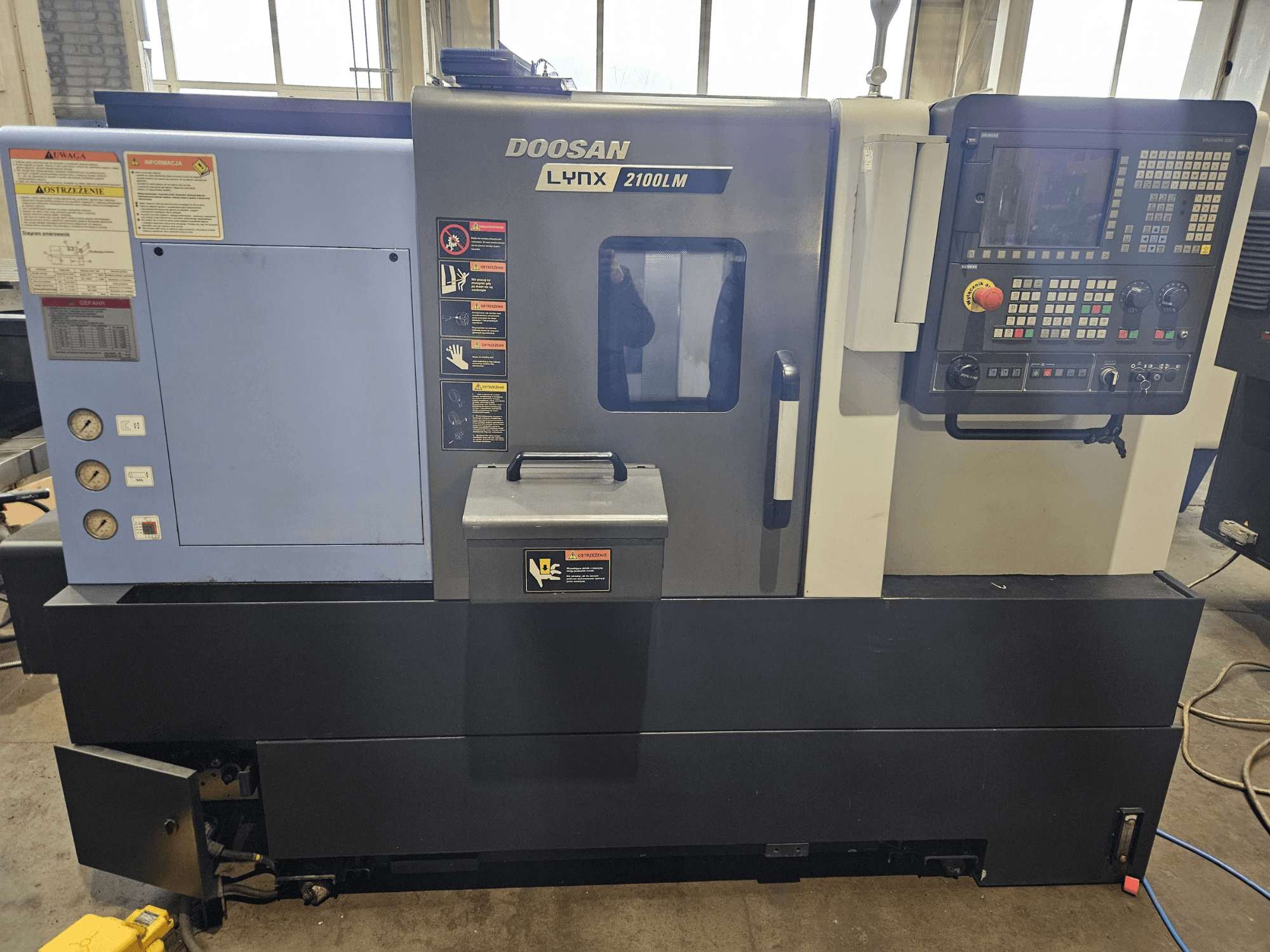 Doosan Lynx 2100LM CNC lathe, front view, with control panel, air pressure gauges, and safety labels visible.
