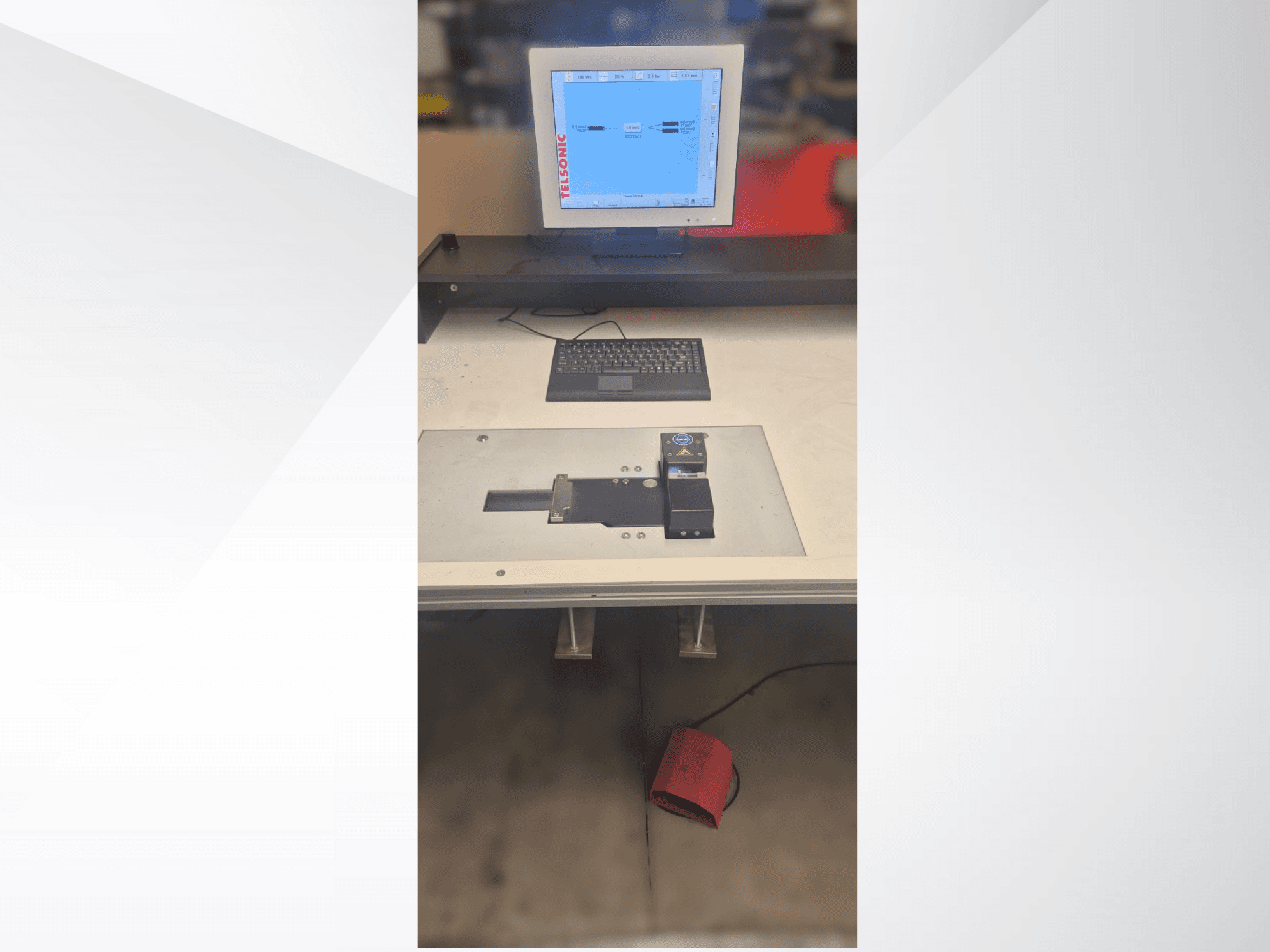 A top-down view of a testing station with a computer monitor, keyboard, and control panel featuring a button and a green light.