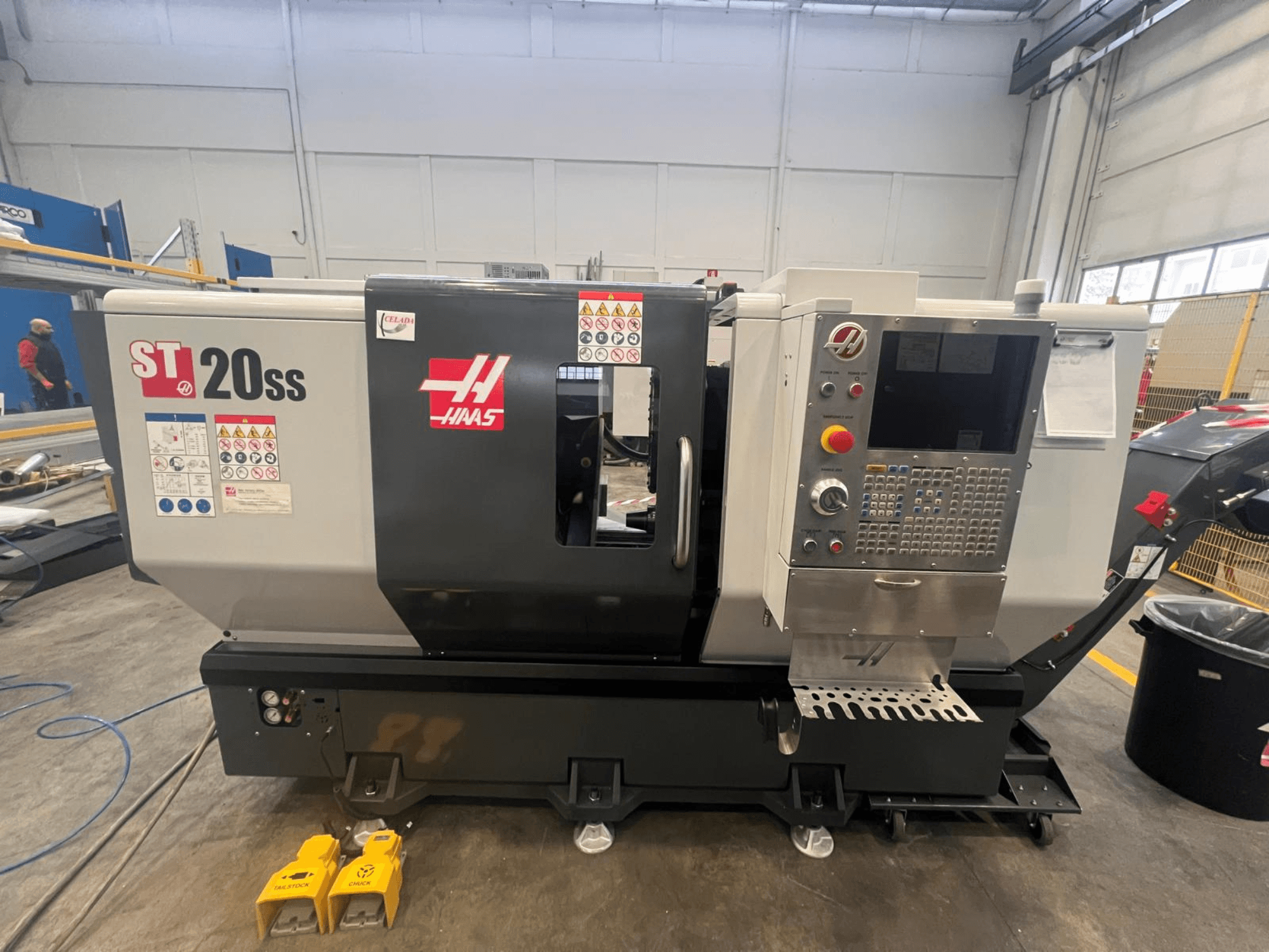 Haas ST 20SS CNC lathe in side view, featuring control panel, safety labels, and foot pedals on the floor.