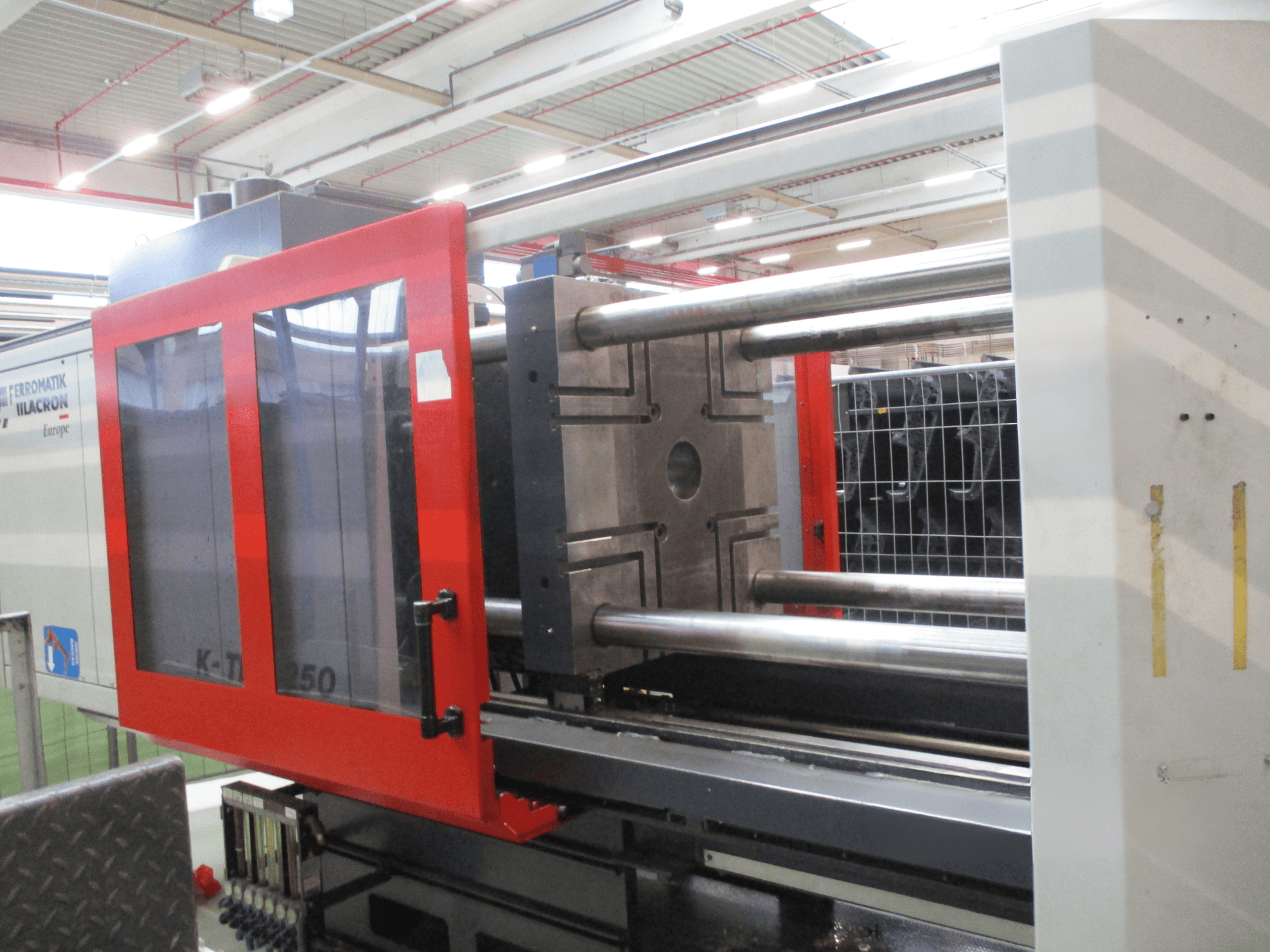 Hydraulic injection moulding machine FERROMATIK K-TEC250S, front view showing red safety door and metallic injection mold.