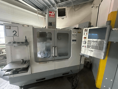 Haas VF-2 CNC machine, front view, featuring controls, tool holder, and clear doors with visible tooling inside the cabinet.