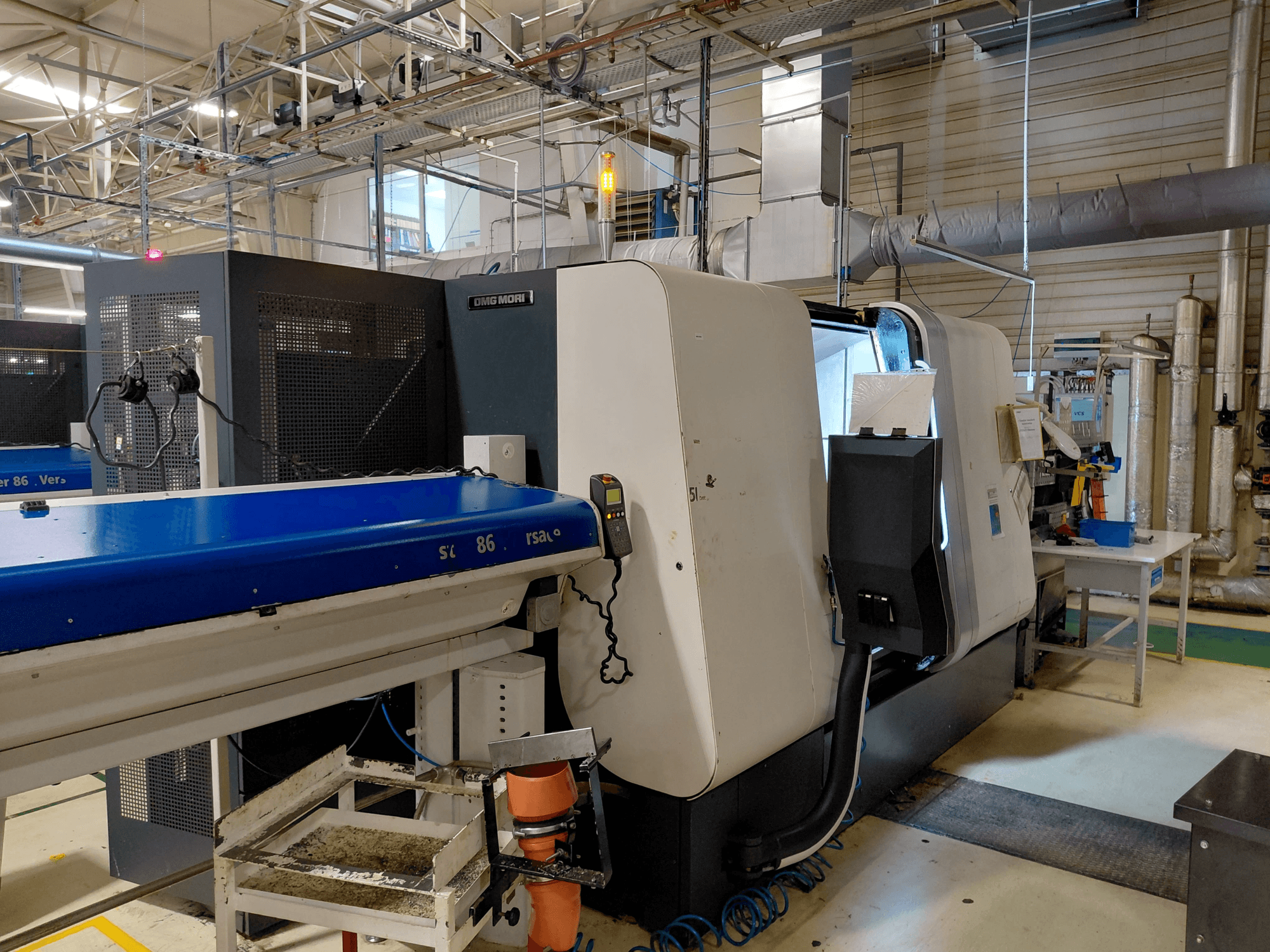 DMG MORI Sprint 65 linear multi-spindle turning machine, side view with control panel and conveyor visible in a workshop setting.