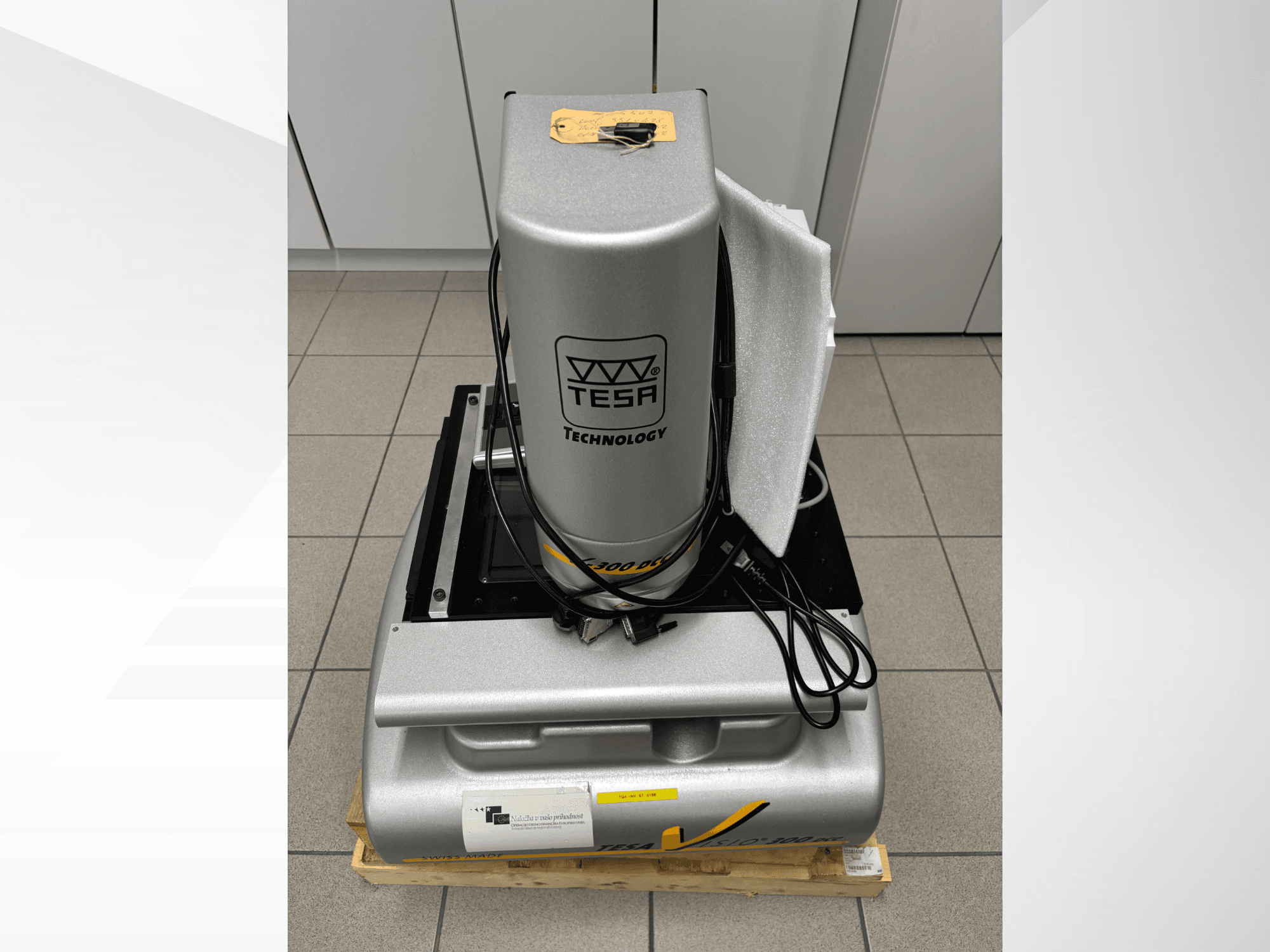 TESA Visio 300 DCC optical measurement machine in a front view with cables, on a wooden pallet, and protective packaging visible.