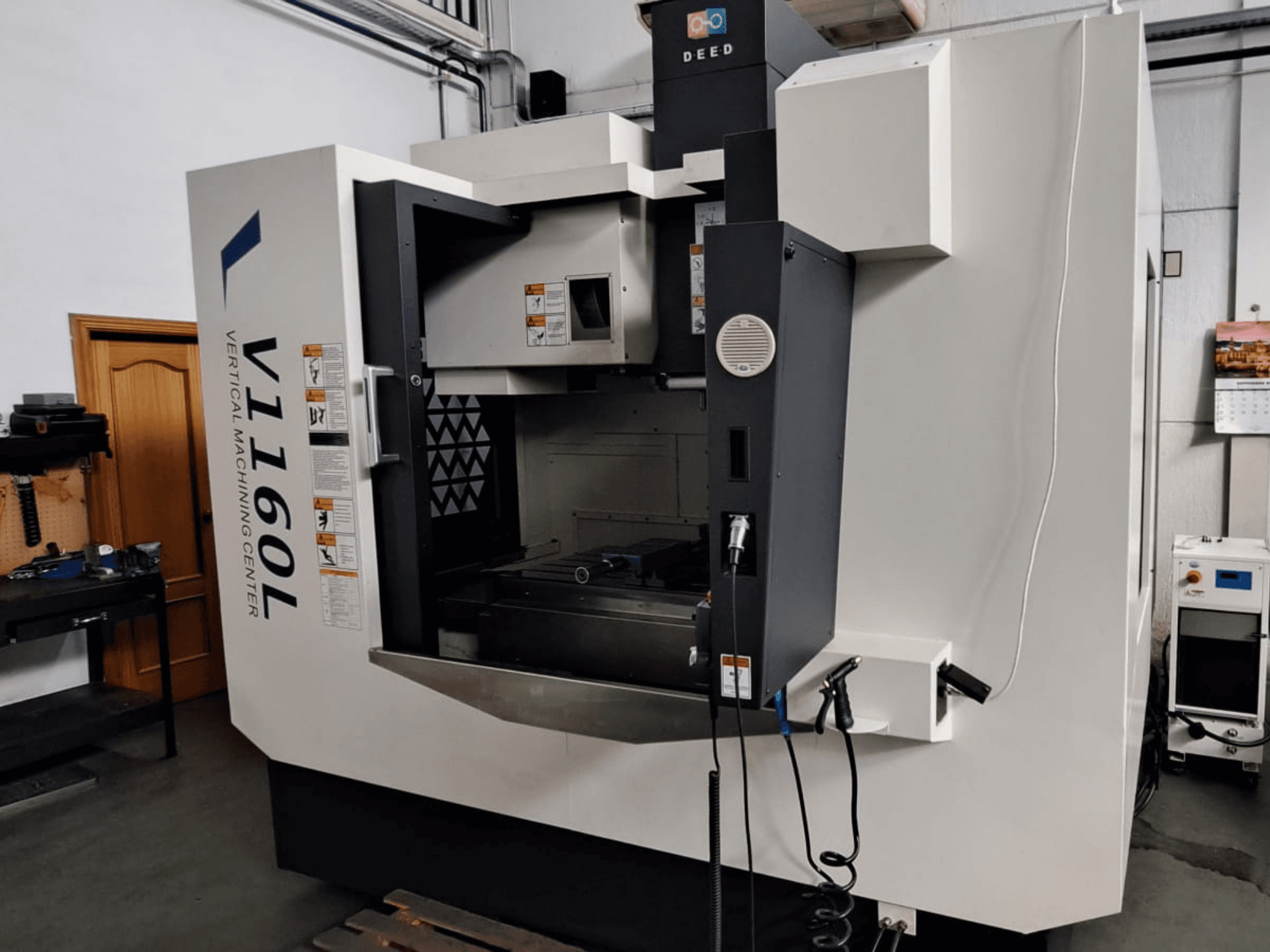 Vertical Machining Center DEED V1160L in front view, showcasing controls and interior setup with tools nearby.