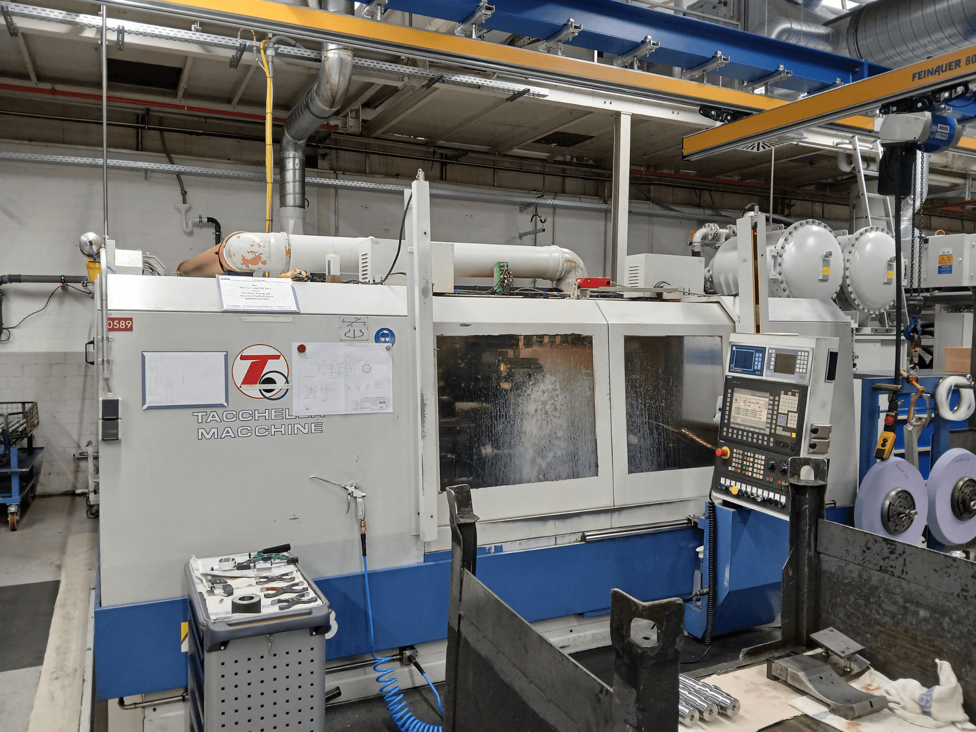 Tacchella machining center from a front view, with control panel and tools visible. Water coolant sprays during operation.