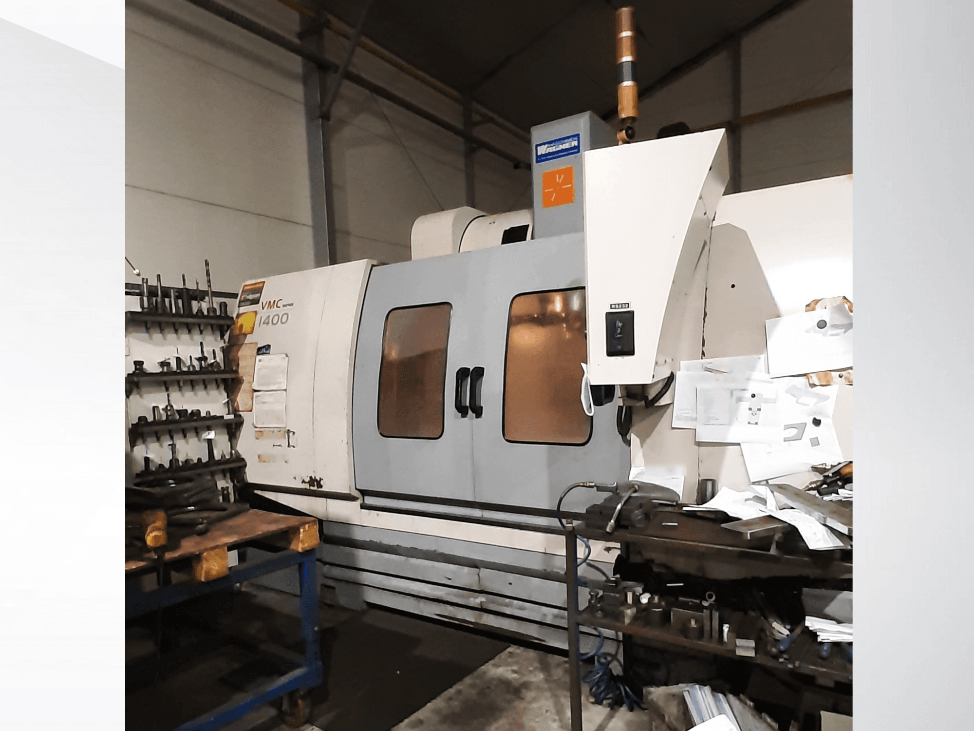 VMC 1400 vertical machining center in side view, featuring control panel, tool rack, and workspace clutter.