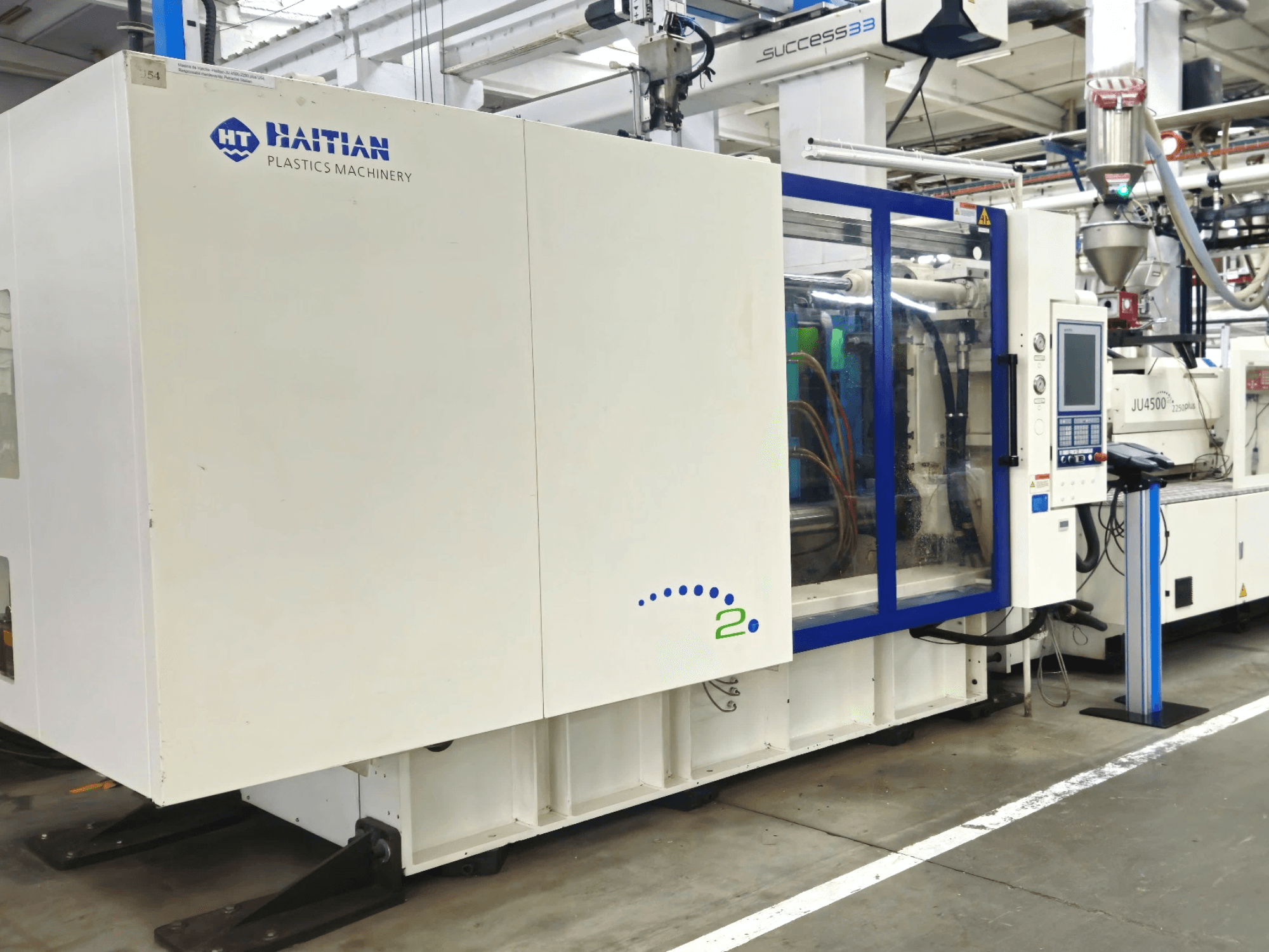 Haitian Plastics Machinery model, front view, showcasing machinery with control panel and visible tubing, in an industrial setting.