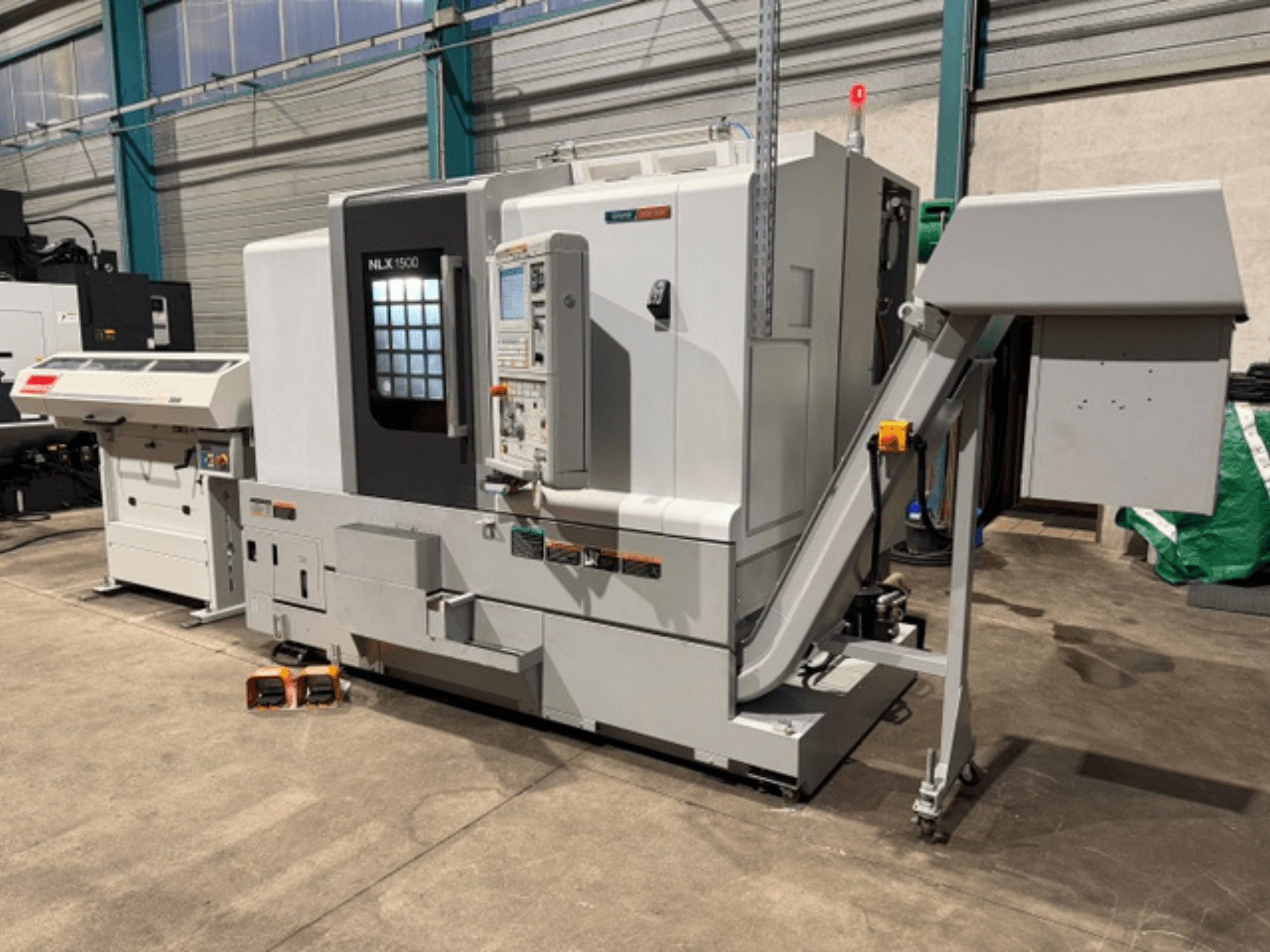 NLK 1500 CNC machine, front view, with control panel and accessory hopper on side, resting on concrete floor.