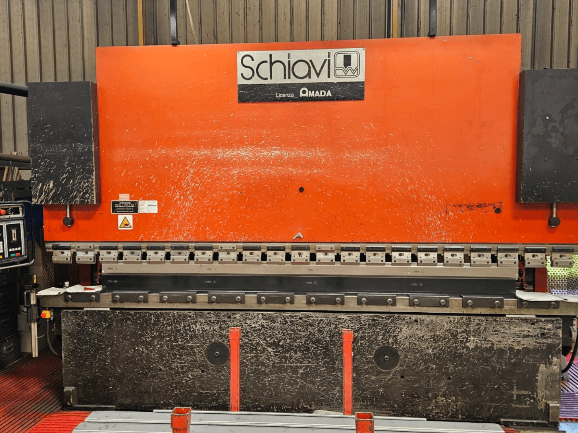 Schiavi Amada metal bending machine, front view, with orange body, control panel on the left, and multiple bending tools visible.