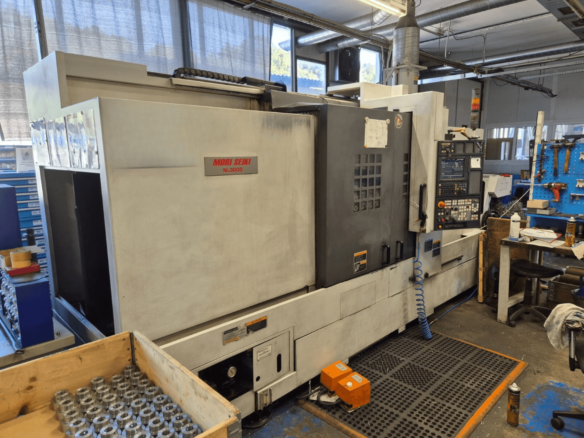 Mori Seiki NL3000 CNC lathe in a workshop, side view showcasing control panel, tools, and metal parts in a wooden box.