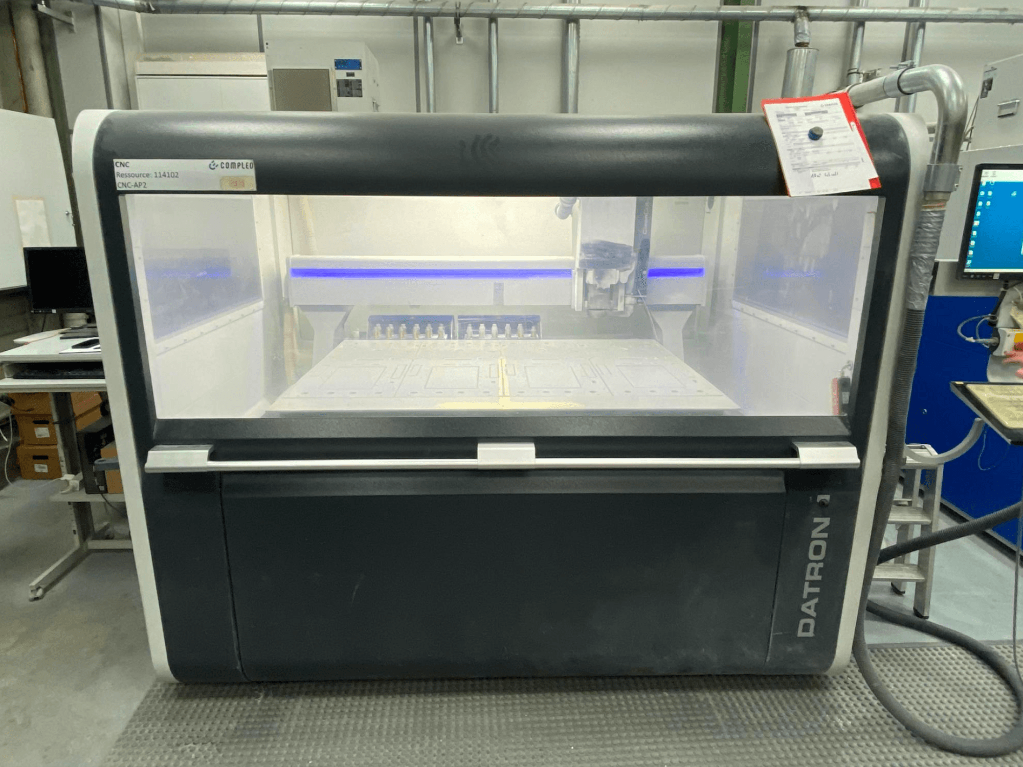 Front view of a Datron MLCube B vertical machining center, with visible controls and a work table, in a workshop setting.