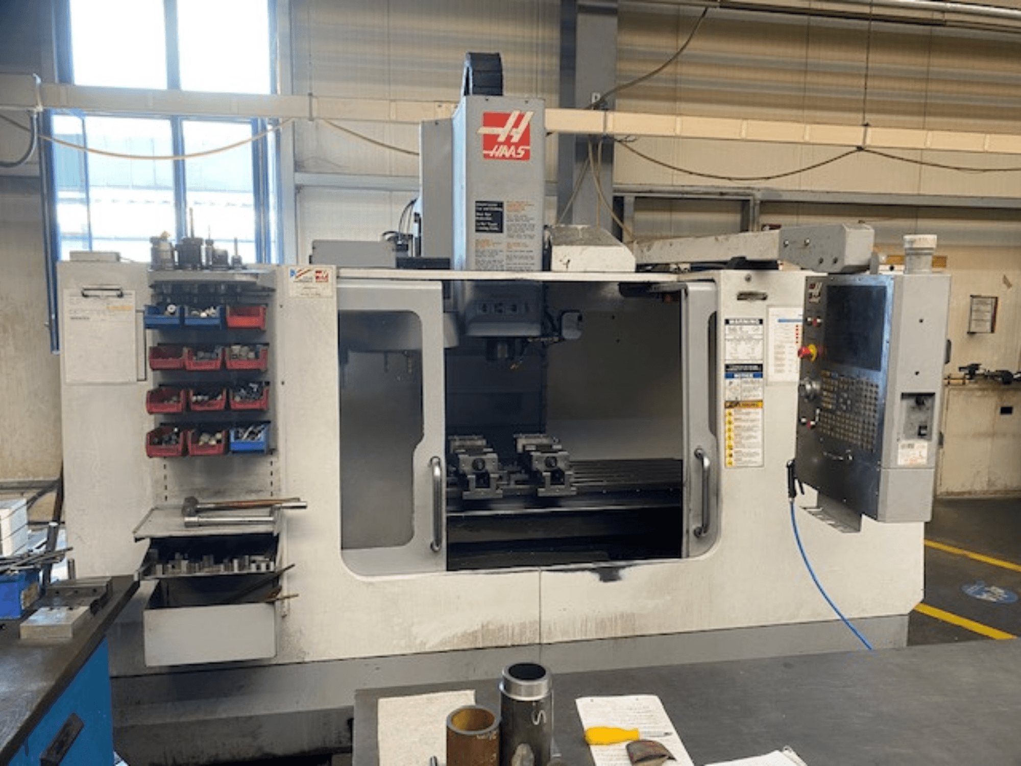 Haas CNC milling machine front view, model VF-2, with tool storage, control panel, and workspace tools visible.