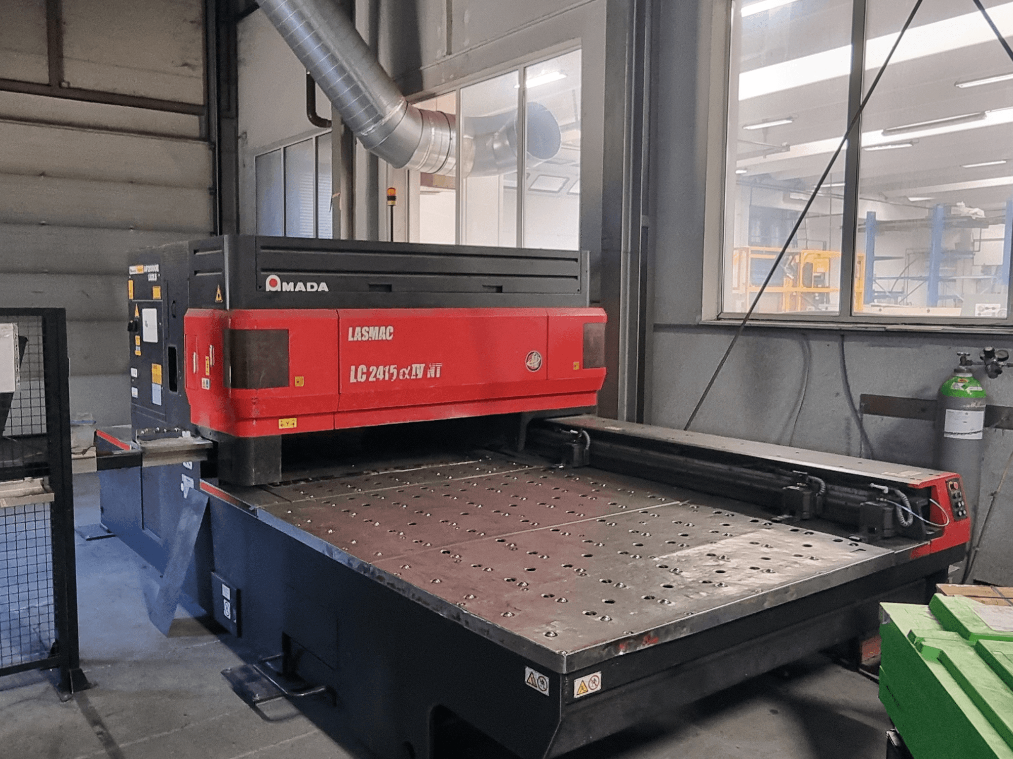 Amada LASMAC LC 2415 αⅡ NT laser cutting machine in red and black, front view, with a powered cutting bed and precision controls.