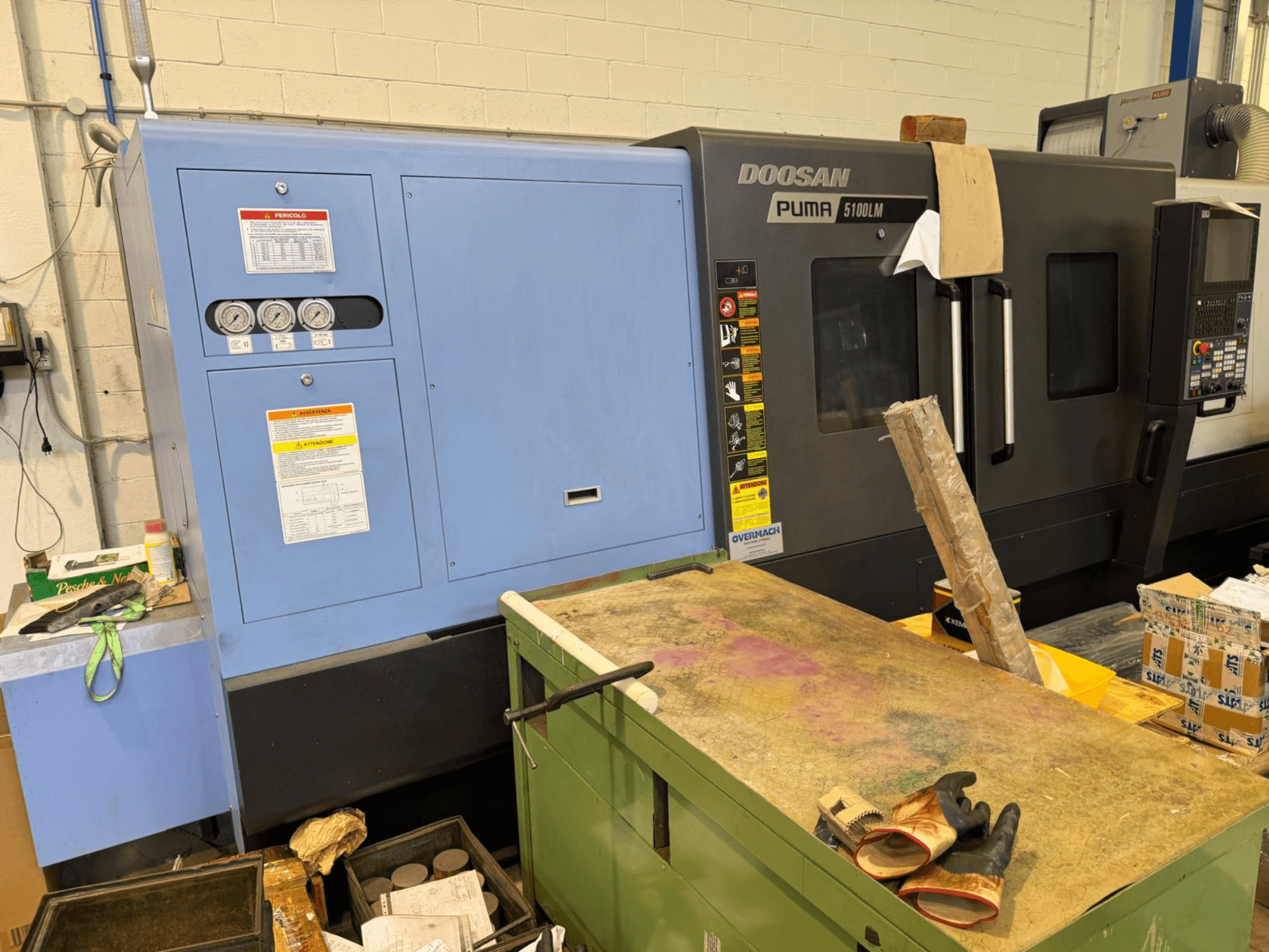 Doosan Puma 5100LM CNC machine and control panel, side view. Gauges and warning labels visible on the blue control unit.