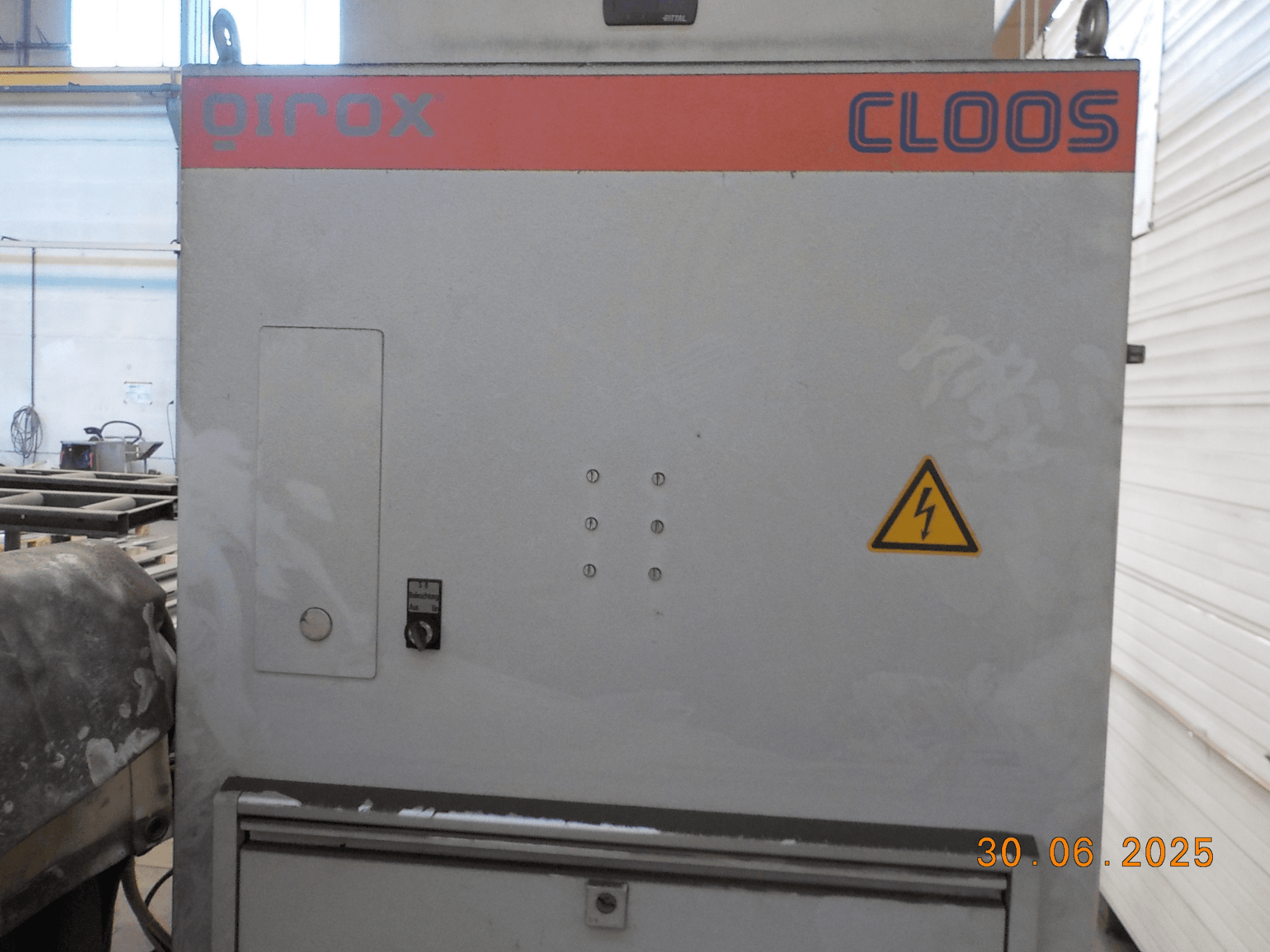 Cloos QIROX welding machine side view, featuring control panel and warning sign, with a dusty surface and visible date stamp.