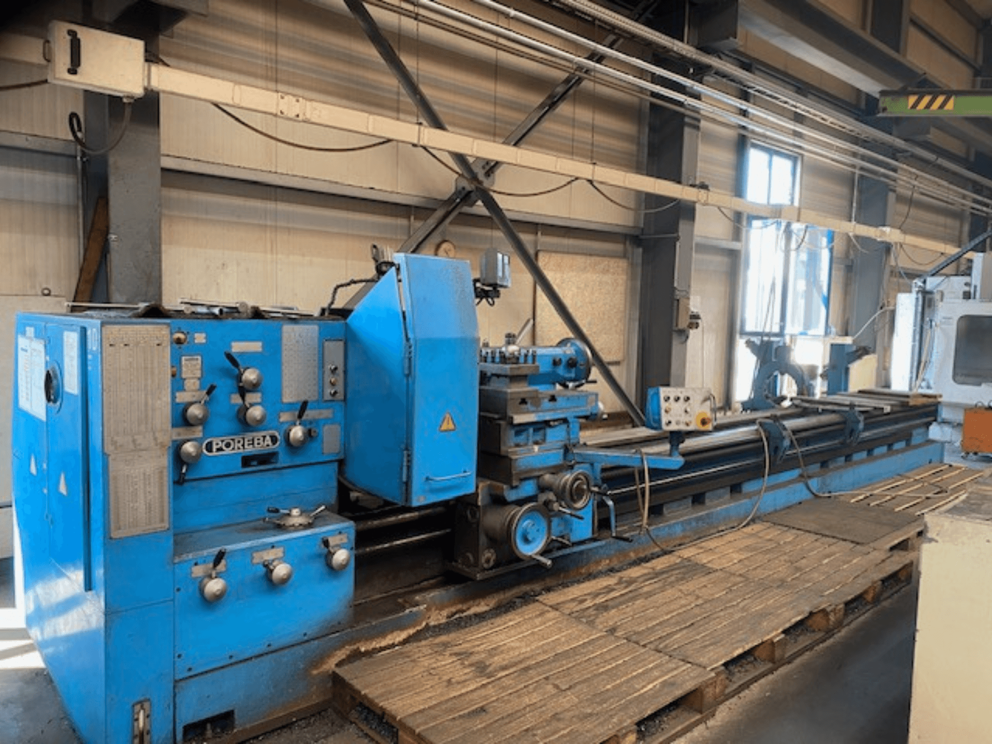 Front view of a blue POREBA lathe machine, featuring control knobs, a tool rest, and wooden pallets underneath.