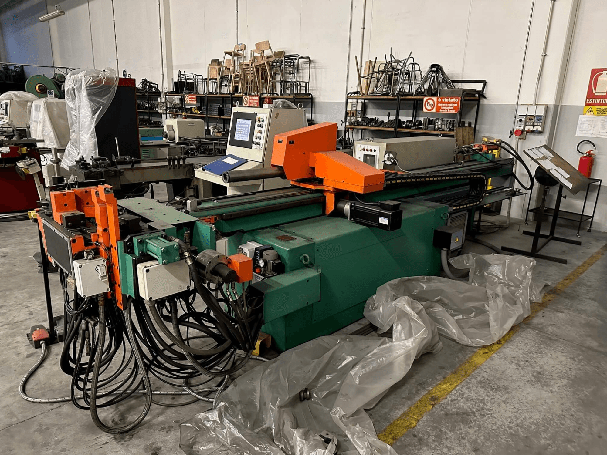 Industrial machine with an orange and green body, control panel, and numerous cables, viewed from the front in a workshop setting.