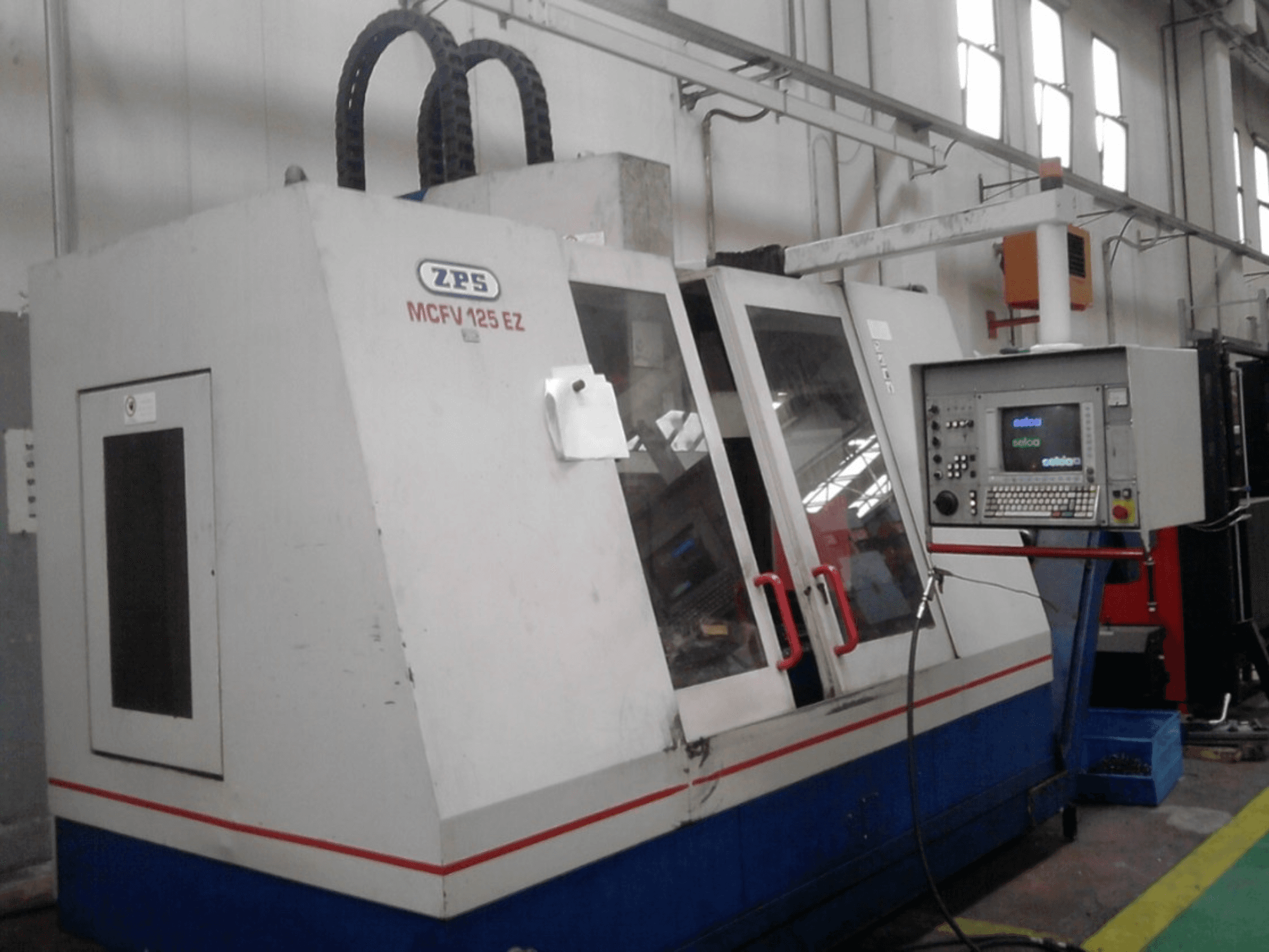 ZPS MCFV 125 EZ CNC machine, front view with control panel and red handles, in a workshop setting with visible hoses.