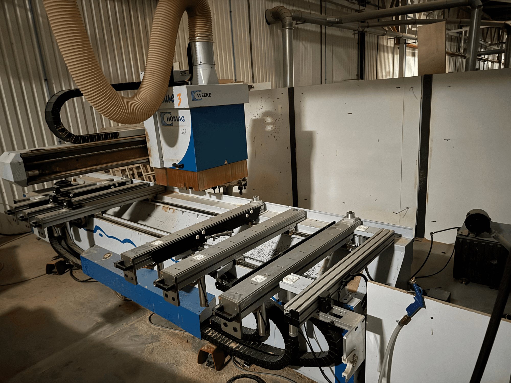 HOMAG CNC machine with a blue and white design, side view, features sliding rails, a dust extraction system, and mounted tools.