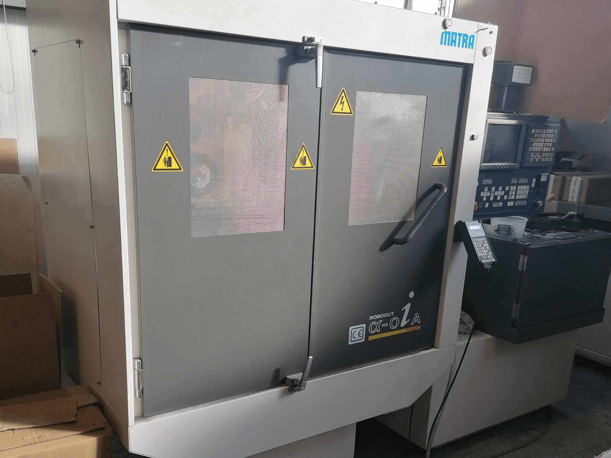 Robocut α-oZα machine by Matra, front view showing safety warnings, control panel, and dual doors with mesh windows.