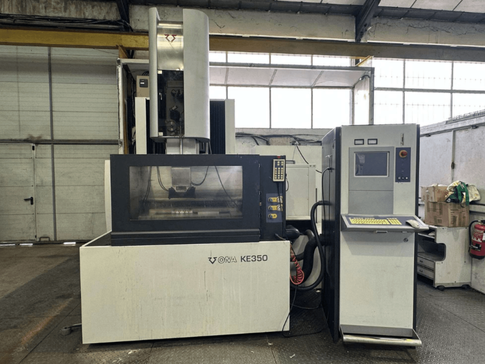 Front view of the ONA KE350 CNC machine with control panel, display screen, and various buttons, located in an industrial setting.