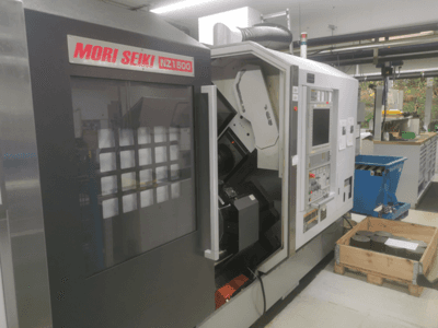MORI SEIKI NZ1500 CNC machine at a slight angle, showing control panel and workspace with metal workpieces on a wooden pallet.