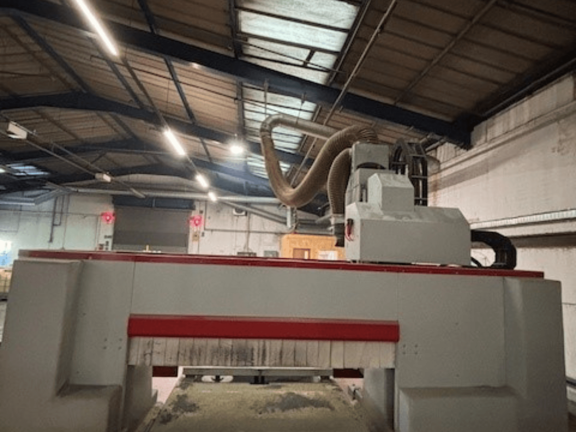CNC router machine in a workshop, side view highlighting the red and gray design, dust extraction system attached.