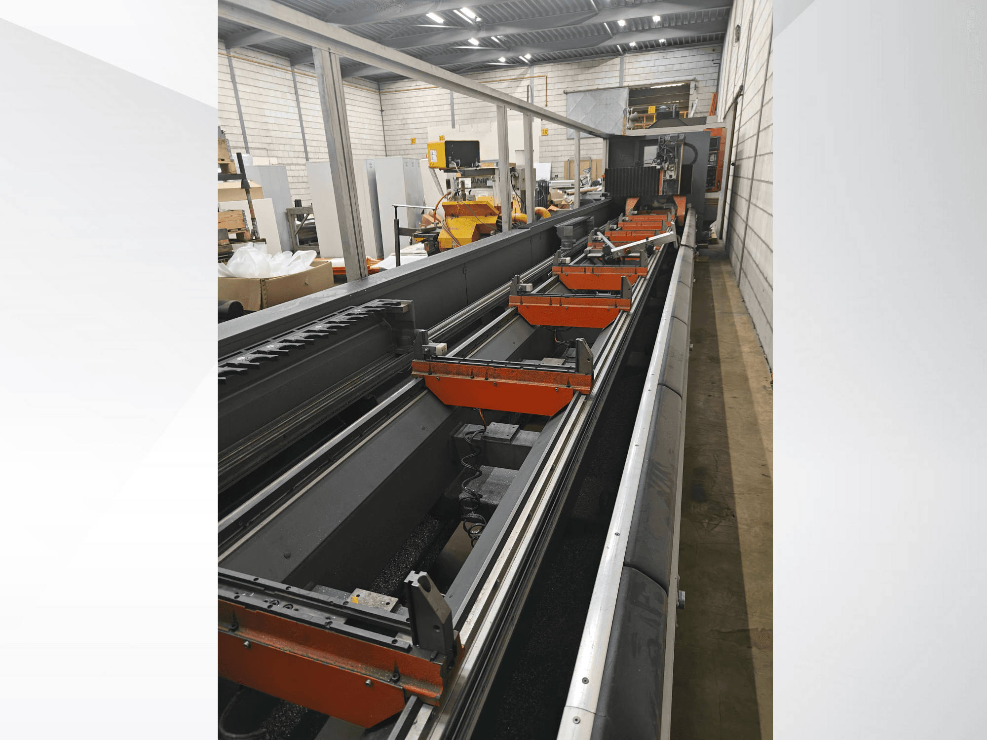 Industrial CNC machine side view, featuring linear rails, orange clamps, and precision components in a warehouse setting.