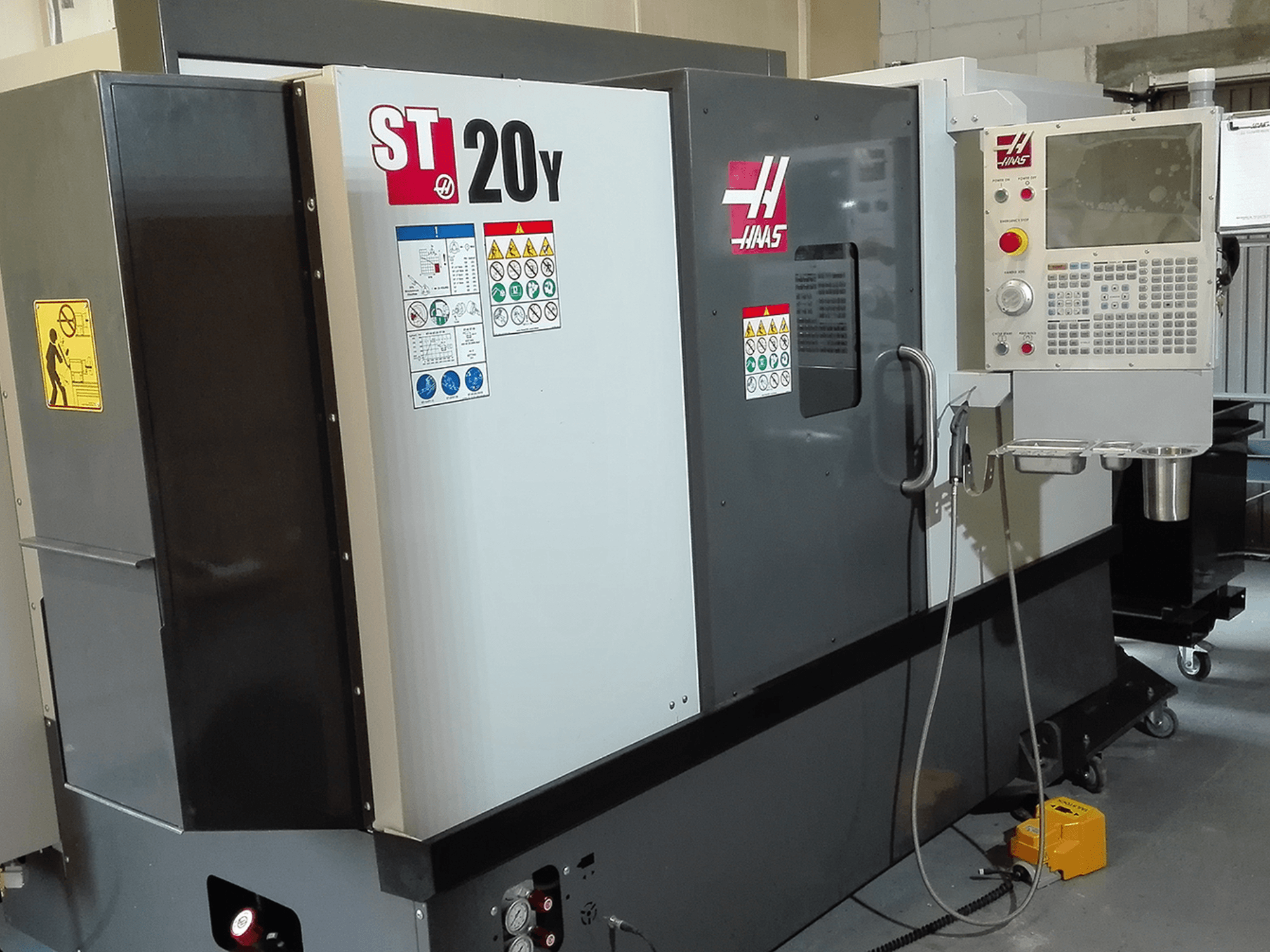 Haas ST20Y CNC lathe in a front view, featuring operation panel, safety labels, and coolant system.