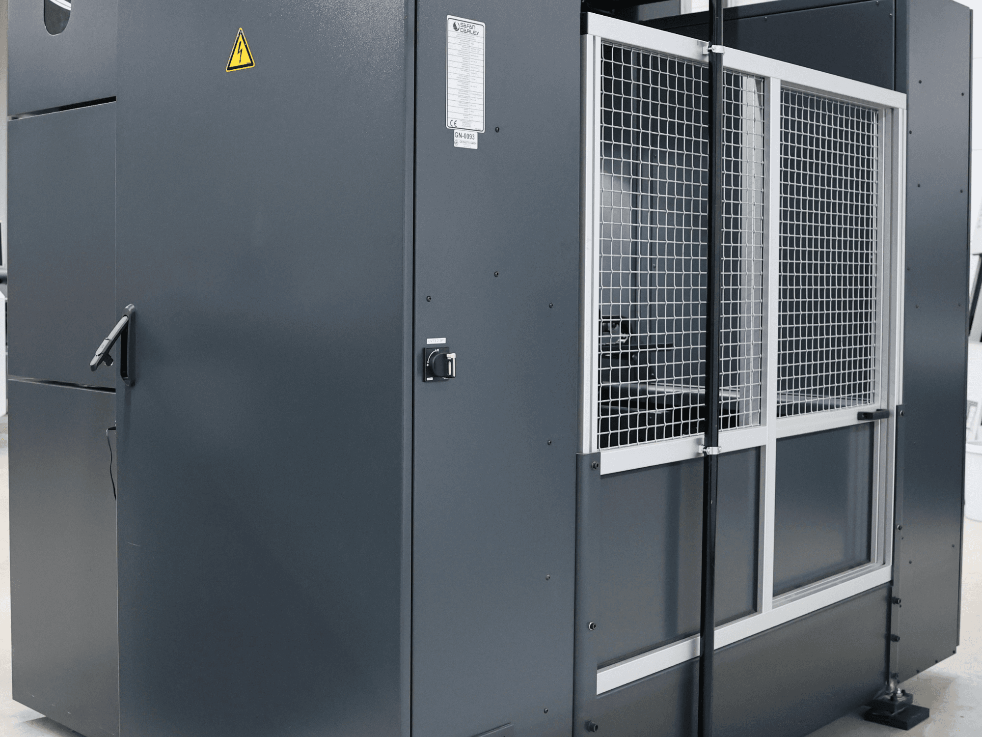 Gray industrial machine with safety warning, front view showing mesh door and control panel, model labeled.