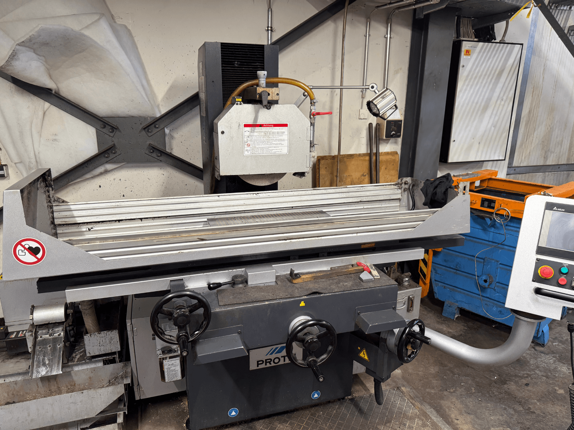 PROTEC machine, front view, showing a surface grinder with manual controls, safety warnings, and a cooling system.