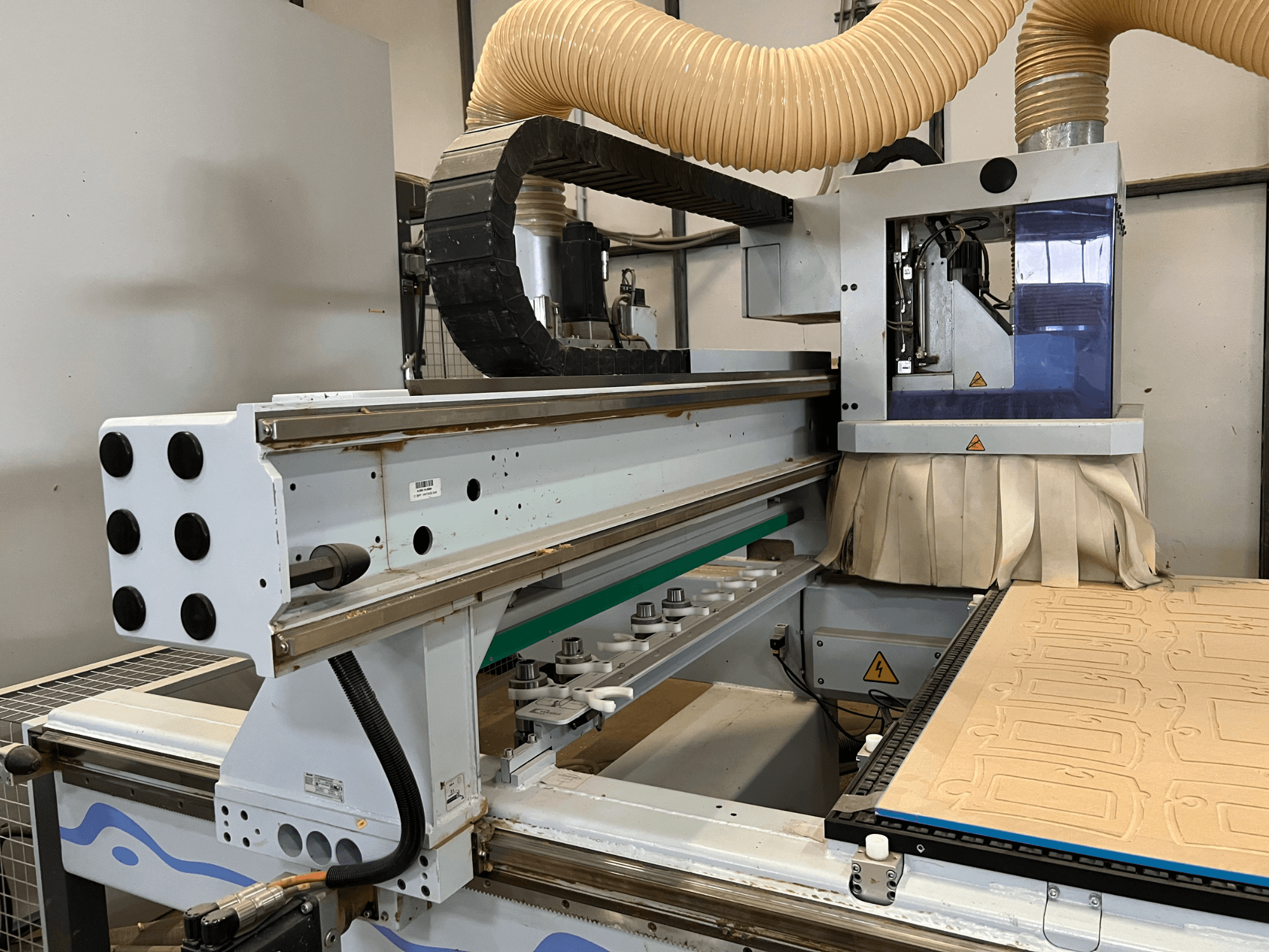Side view of a CNC router with a blue and silver control panel, equipped with dust extraction and a wood cutting bed.