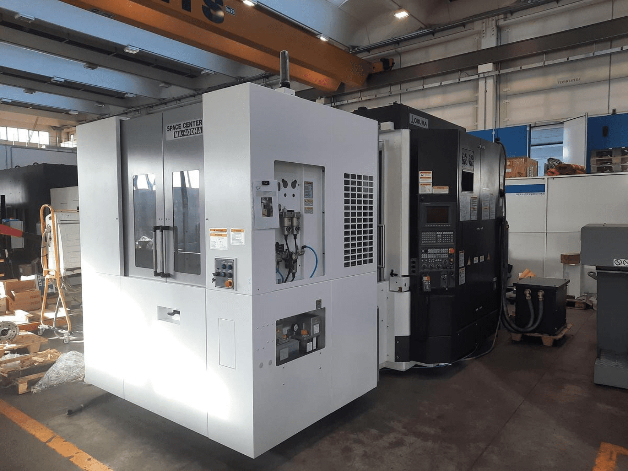Front view of SPACE CENTER IM-400HAA and OKUMA CNC machines, showcasing various controls and manufacturer labels.