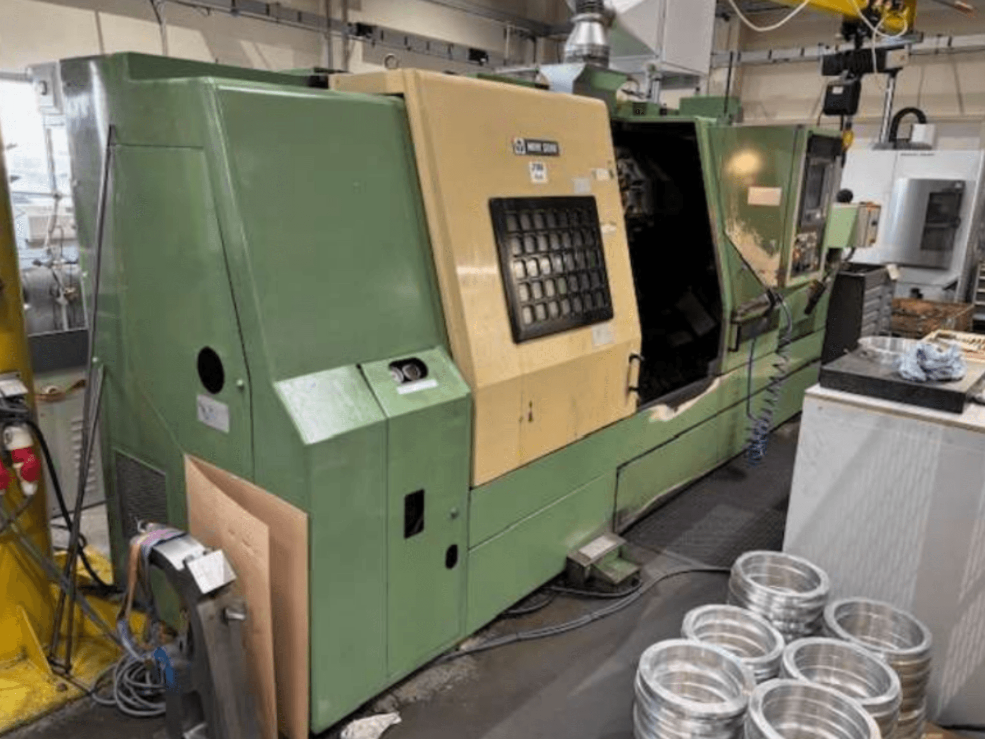 Green CNC lathe machine from Mazak, viewed from the front, showcasing a control panel and machined aluminum parts on a worktable.