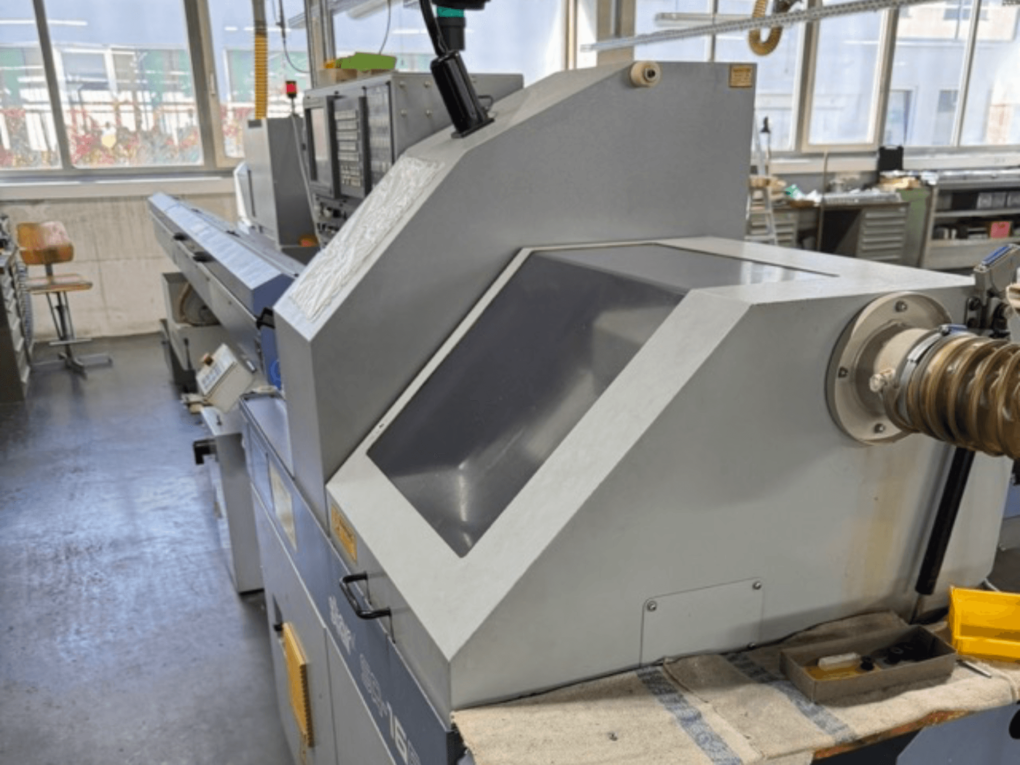 Gray industrial machine viewed from the side, features a large angled panel, control buttons, and a hose attachment.