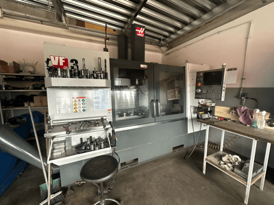 Haas VF-3 CNC machine in workshop, front view with tools and controls on adjacent table, displaying technical interface and safety info.