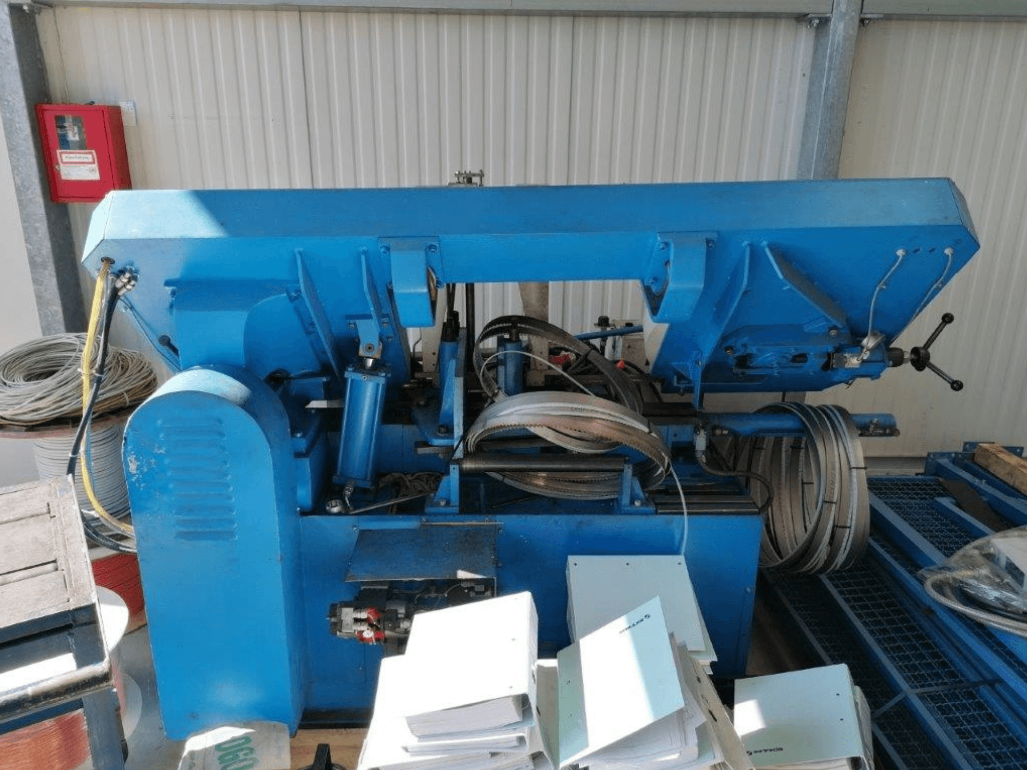 Blue industrial machine with hydraulic components, side view, includes hoses and sheets of metal on a surface.