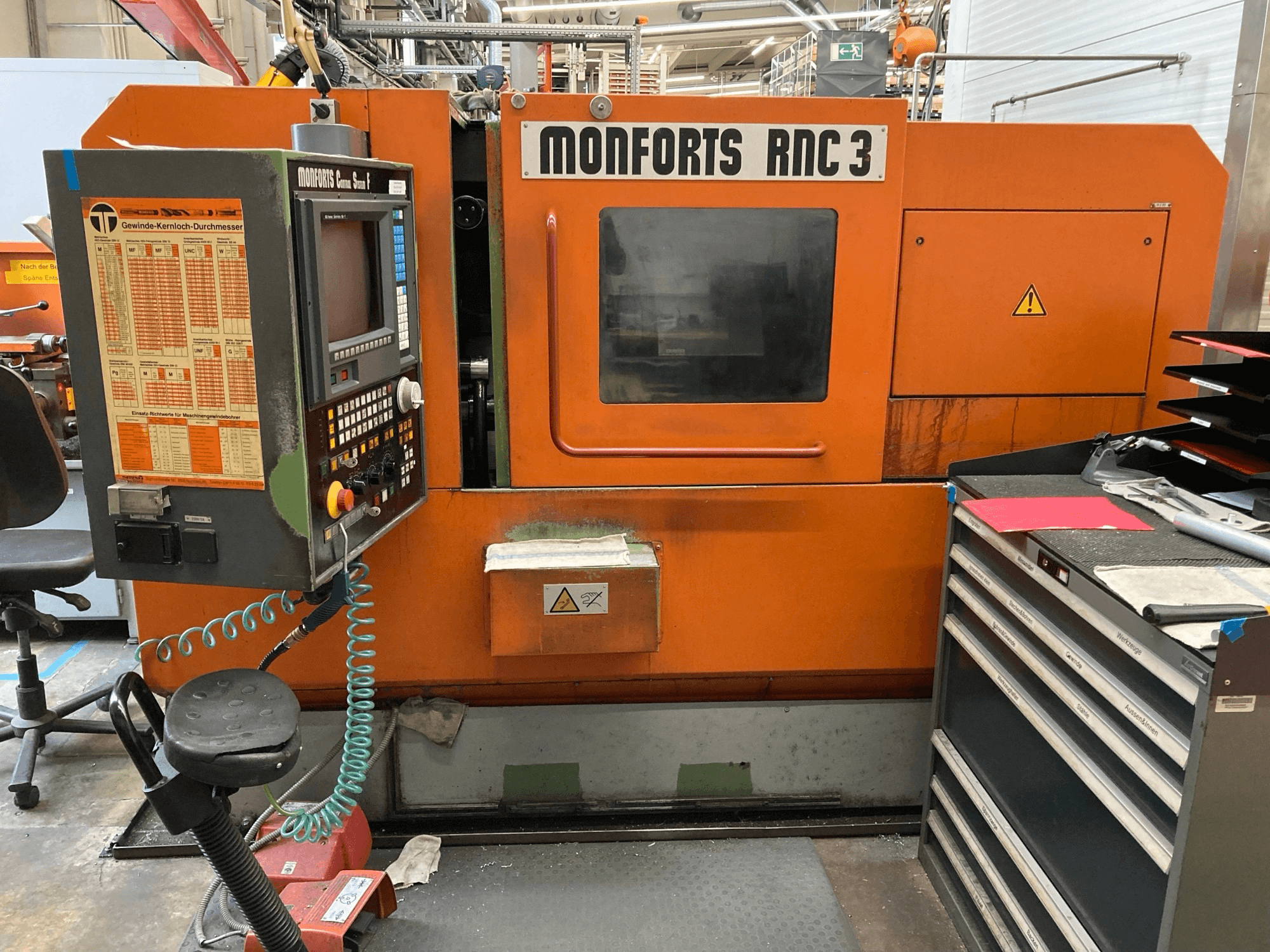Monforts RNC 3 machine in orange and black, front view, featuring a control panel and various tool drawers.